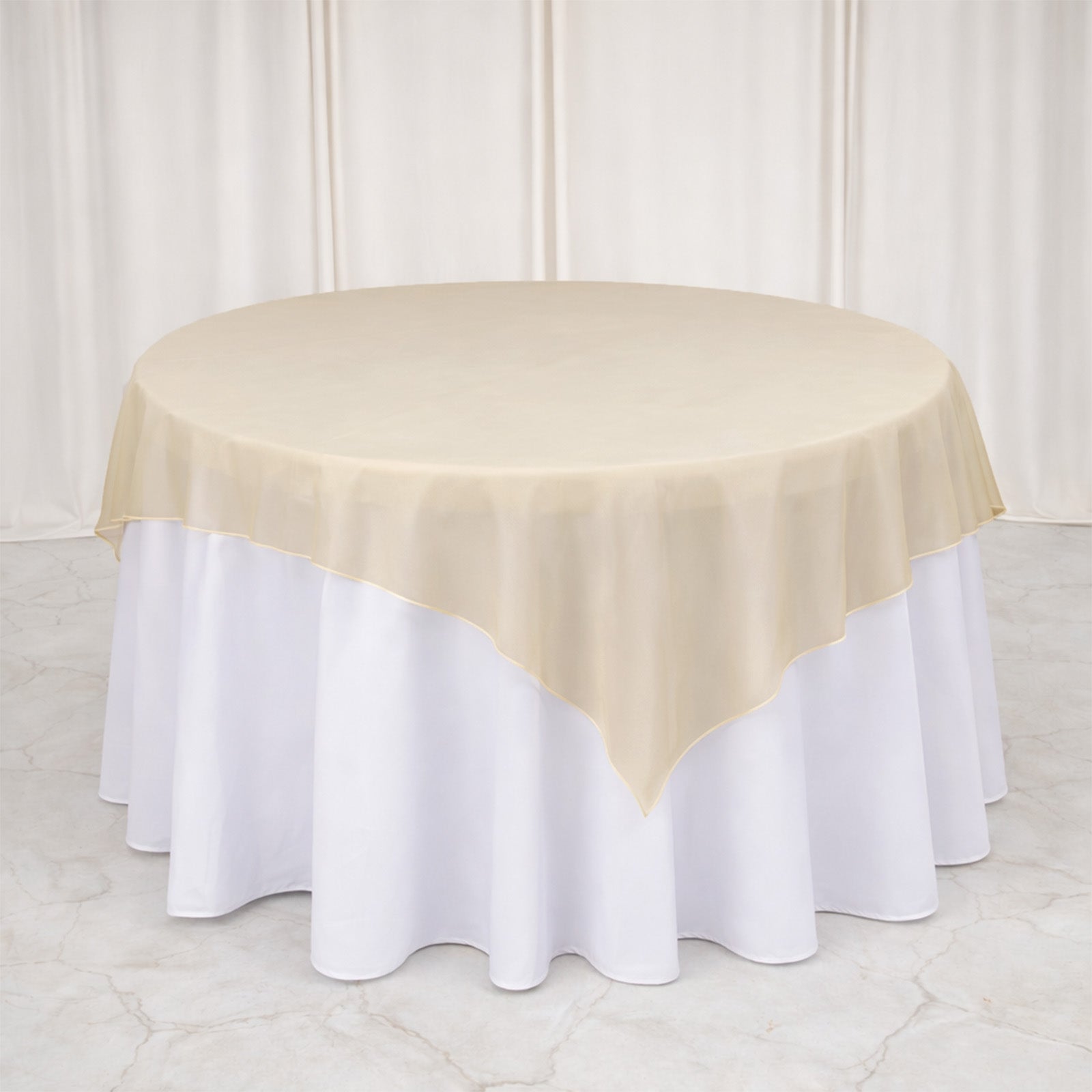 Gold organza table overlay on a round table with a white tablecloth.