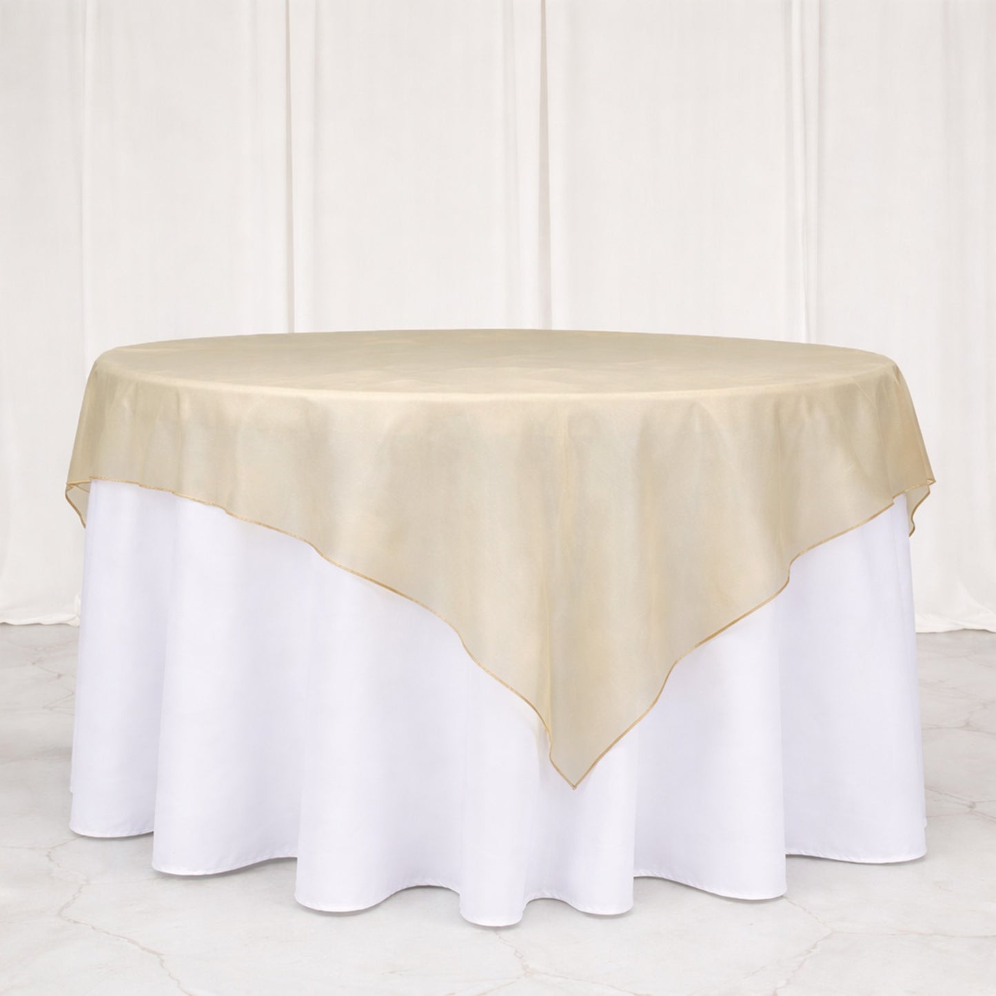 Beige organza table overlay on a round table with white tablecloth.
