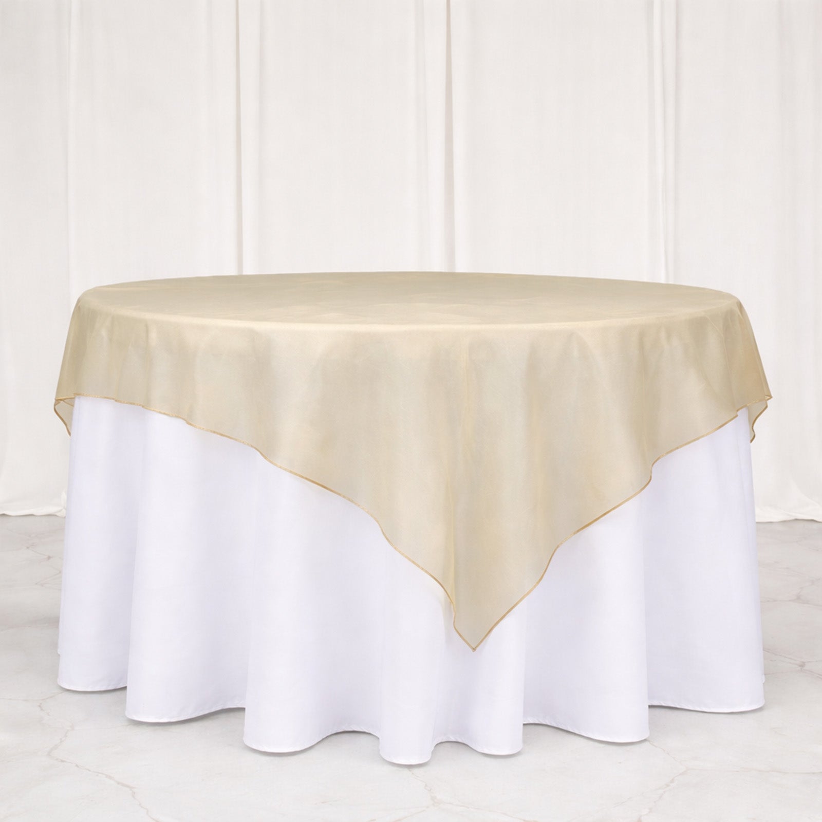 Beige organza table overlay on a round table with white tablecloth.