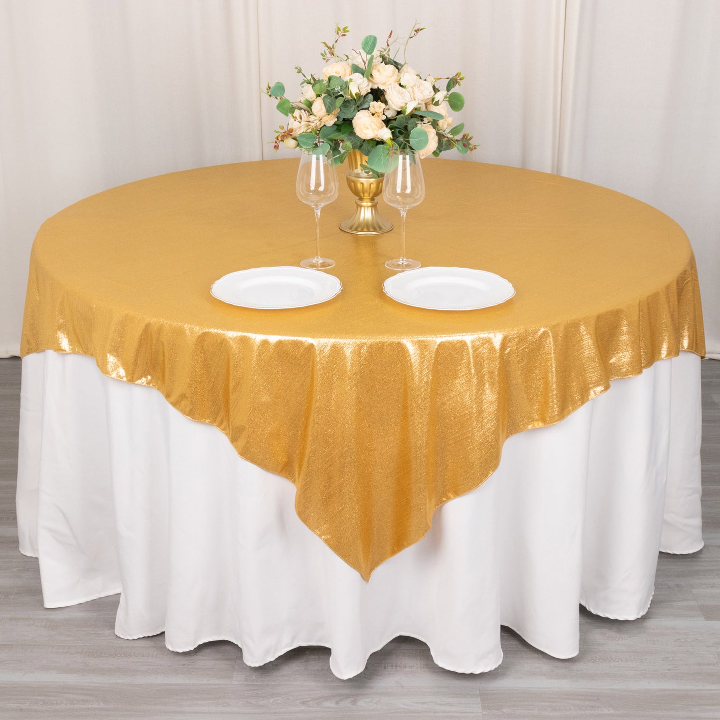 Gold shimmer sequin table overlay on a round table with floral arrangement.