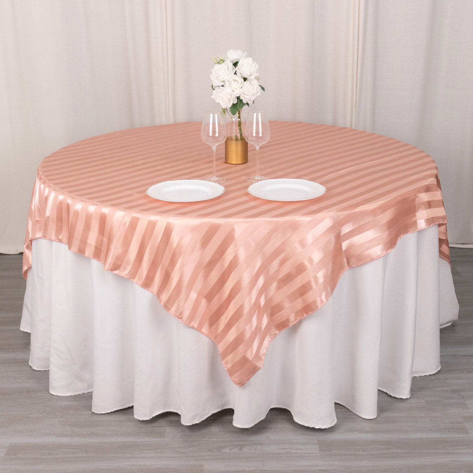 Dusty rose satin stripe table overlay on a round table with white linens.