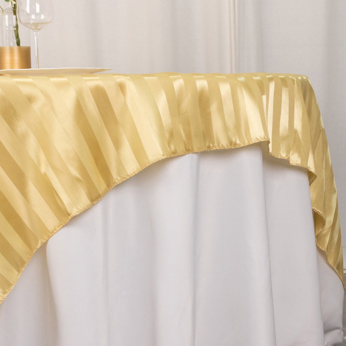 Champagne satin stripe square table overlay on a white tablecloth.