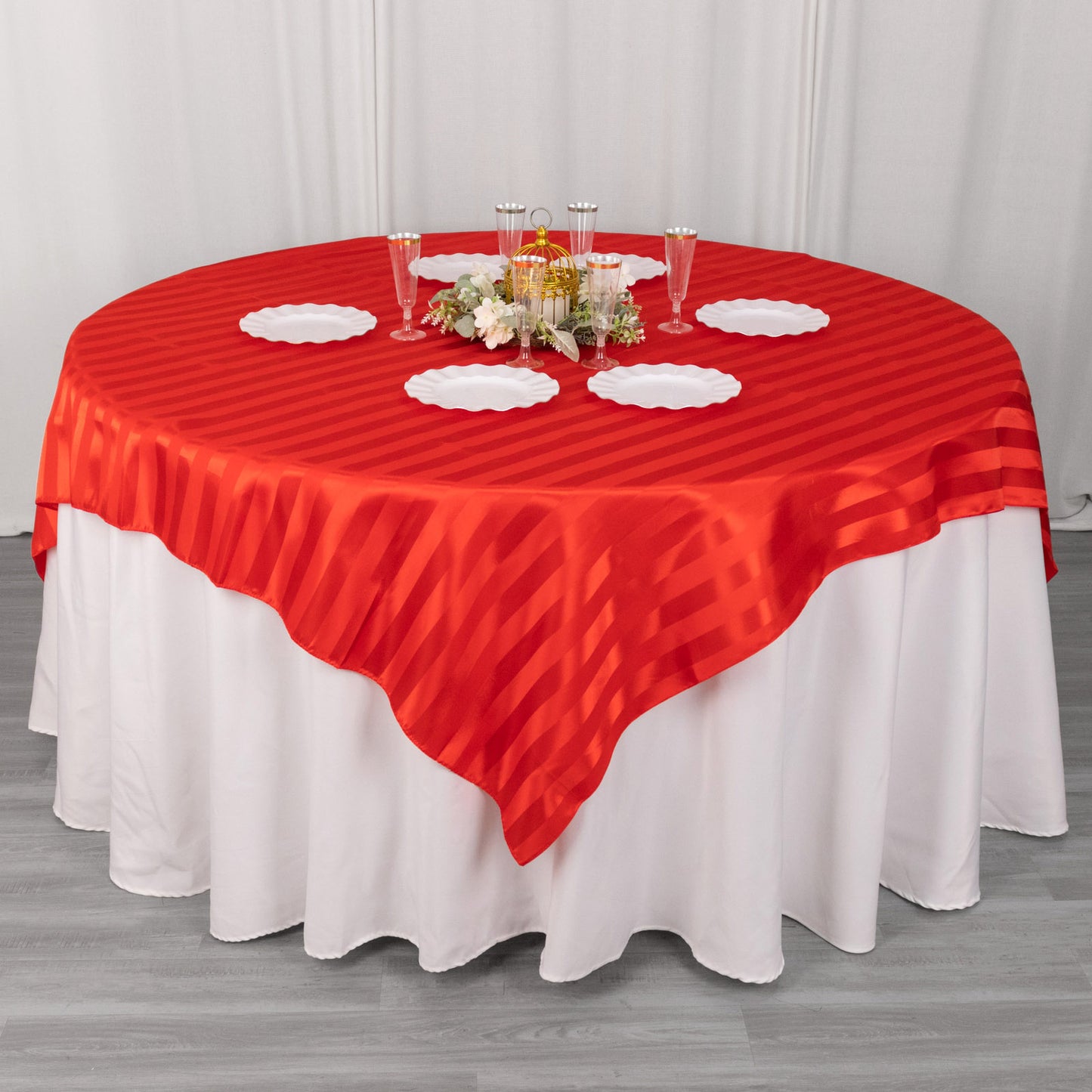 Red satin stripe table overlay on a round table with elegant decor.