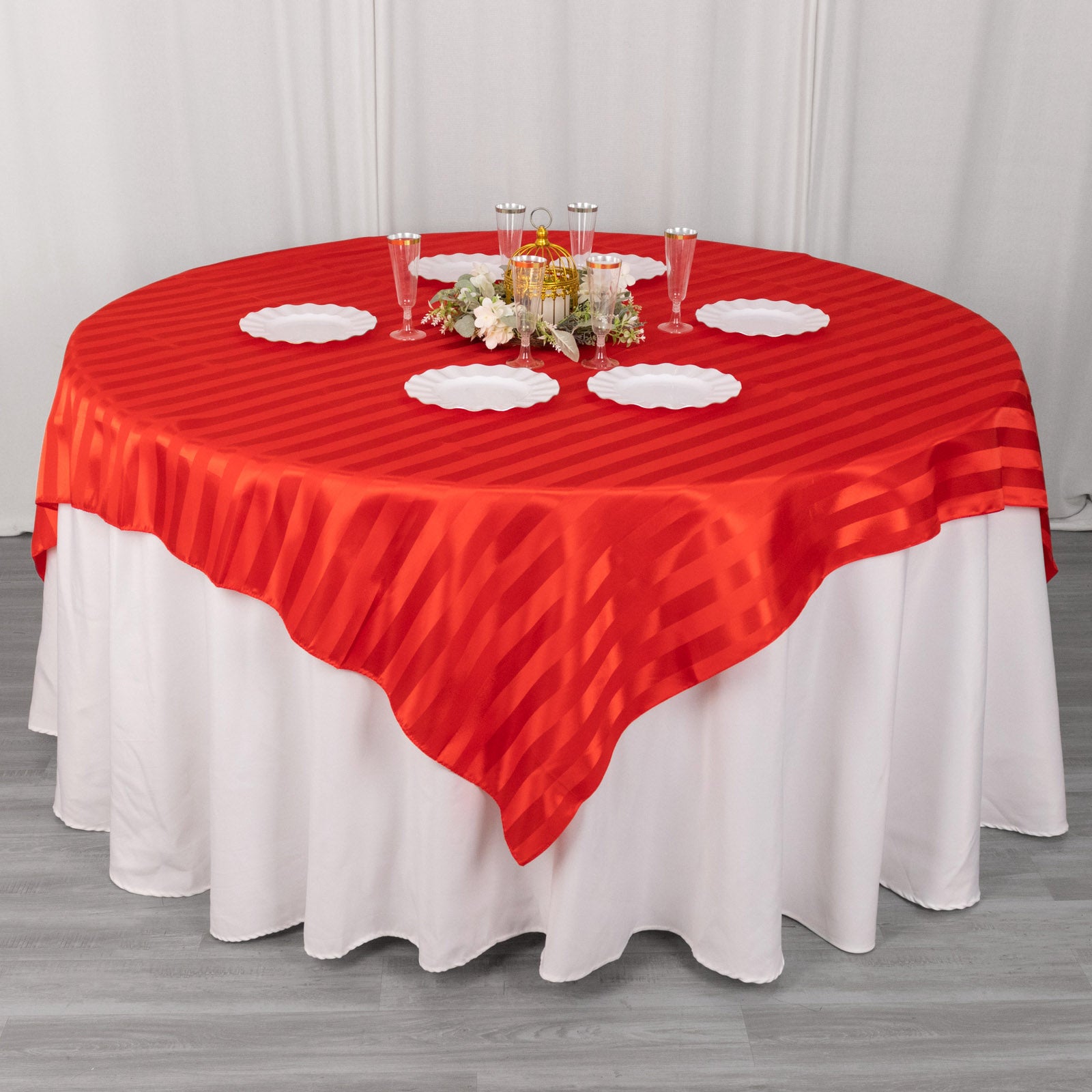 Red satin stripe table overlay on a round table with elegant decor.