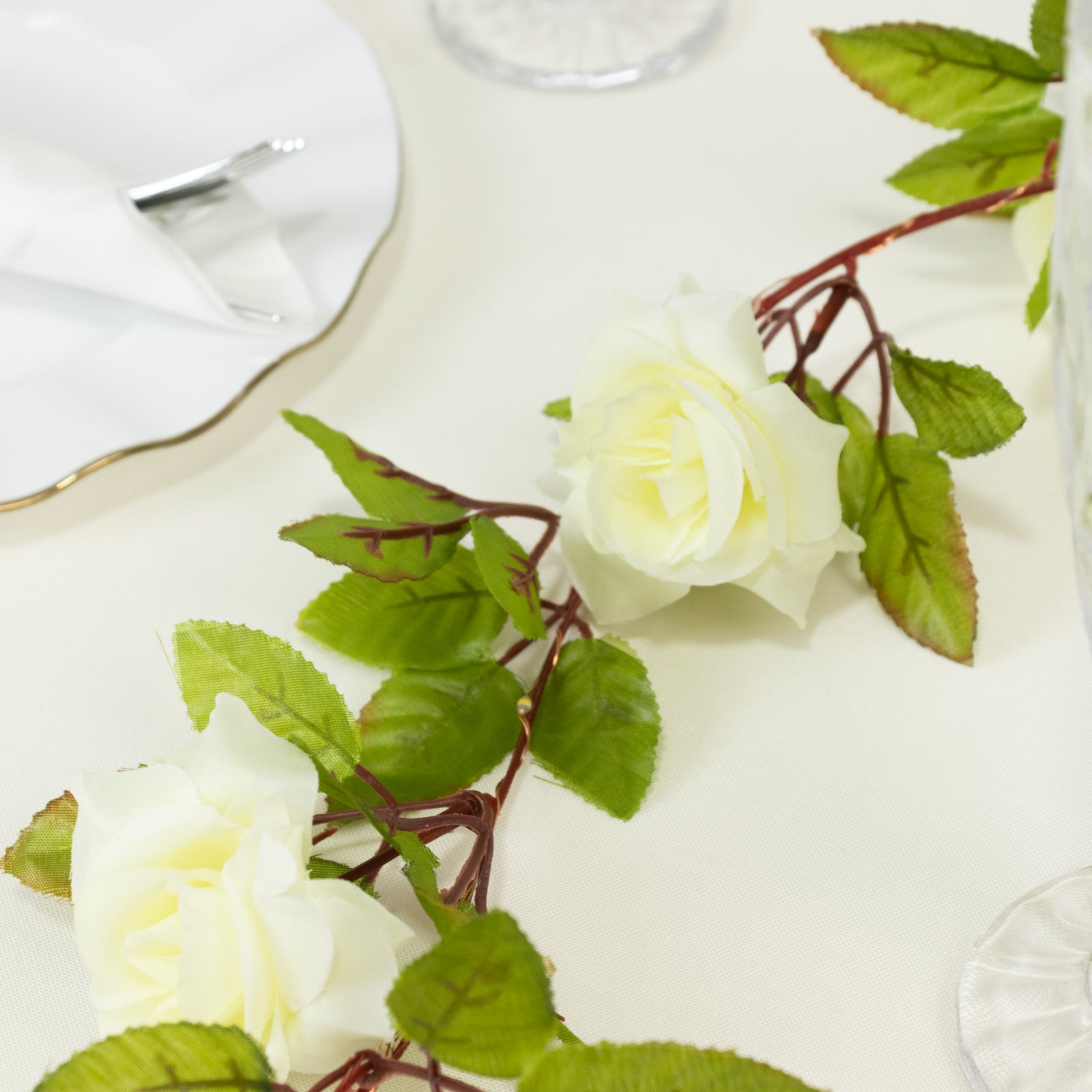 Warm white silk rose flower garland with green leaves and string lights.