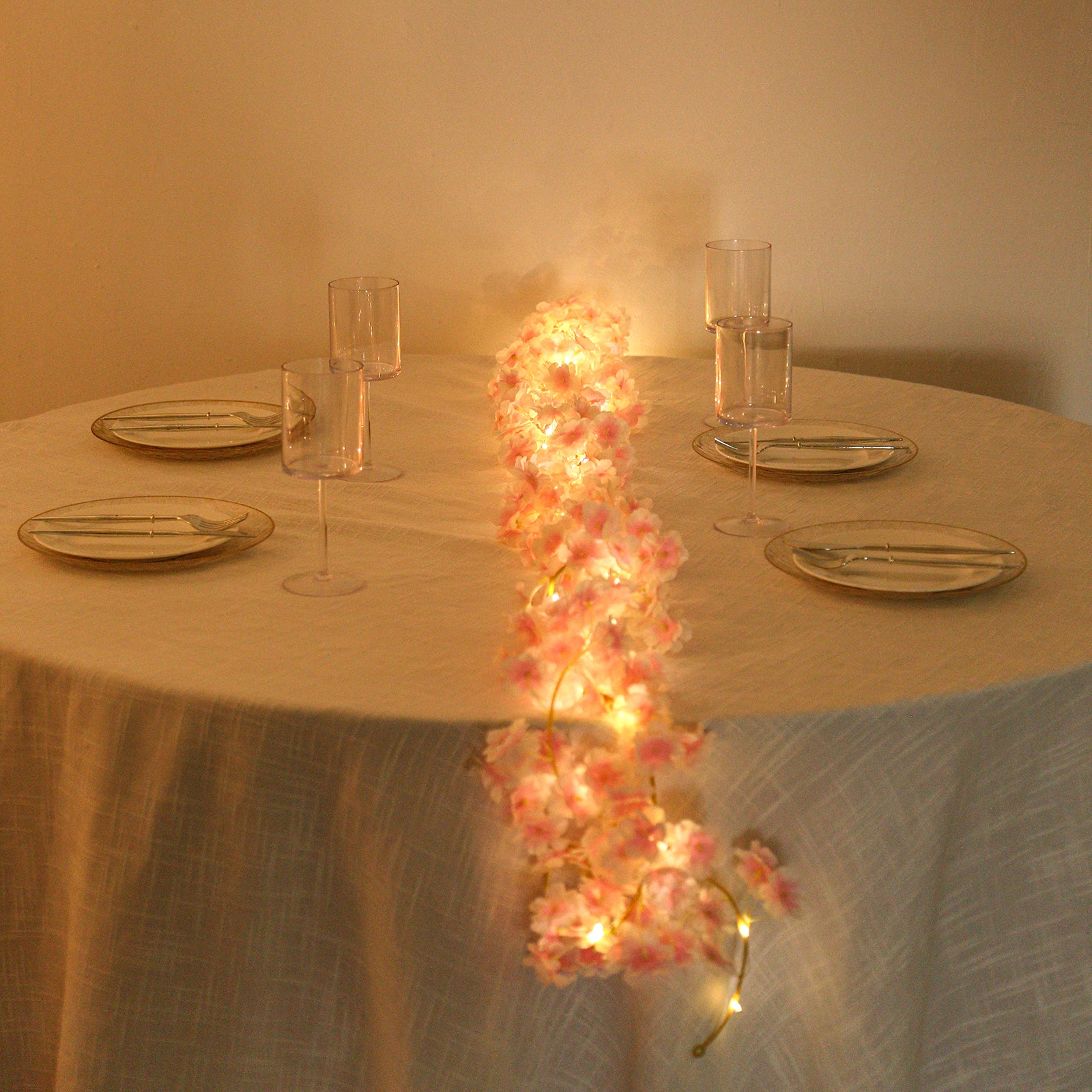 Blush artificial cherry blossom garland LED string lights on a table.