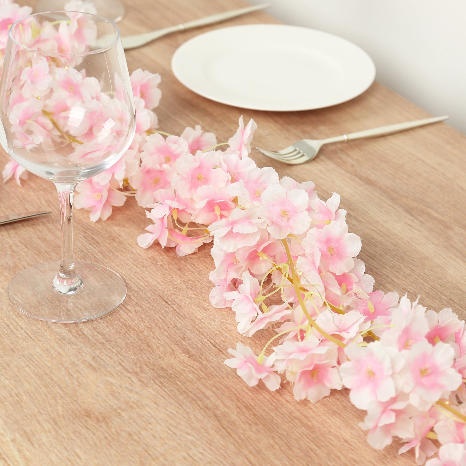 Blush artificial cherry blossom garland string lights on a wooden table.