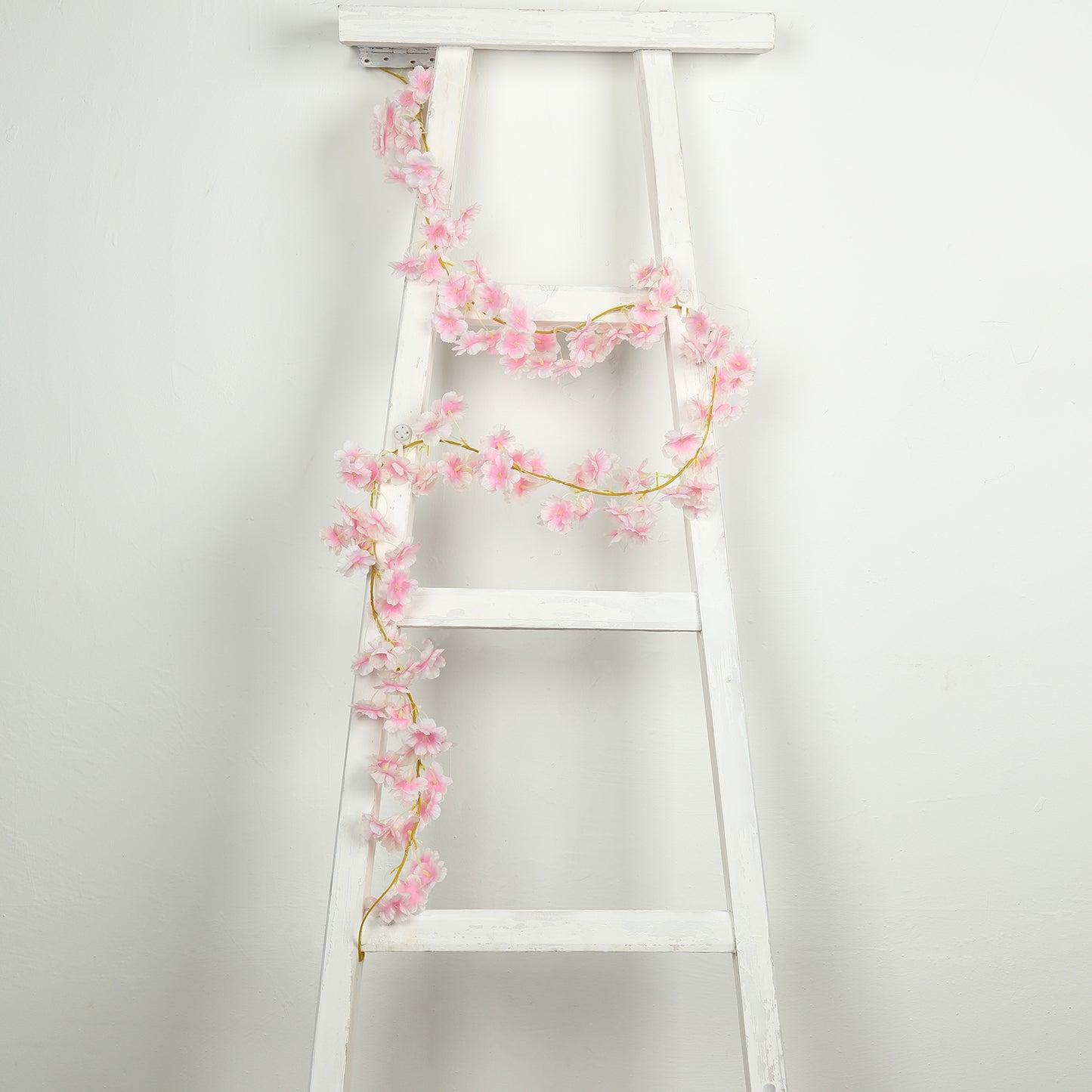 Blush artificial cherry blossom garland LED string lights on a white ladder.