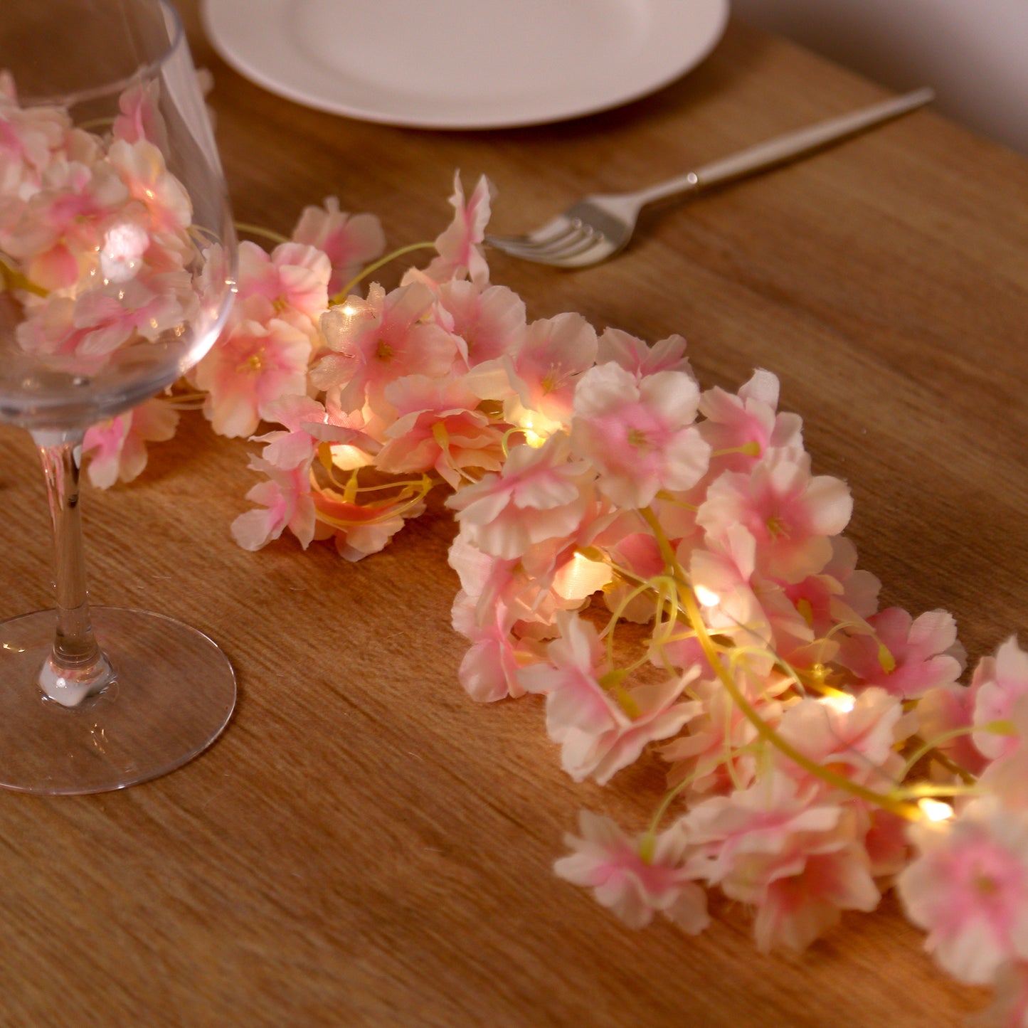 Blush cherry blossom garland LED string lights on a wooden table.