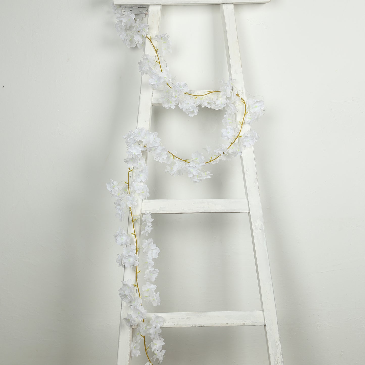 White artificial cherry blossom garland LED string lights on a ladder.