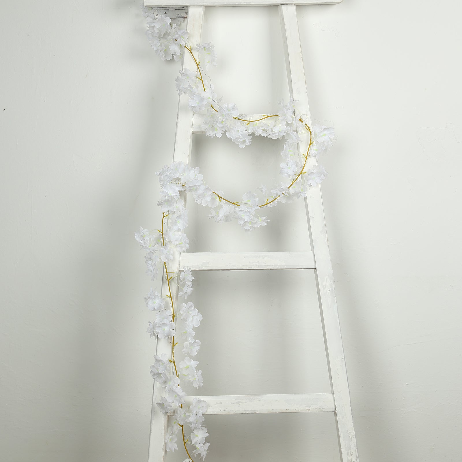 White artificial cherry blossom garland LED string lights on a ladder.
