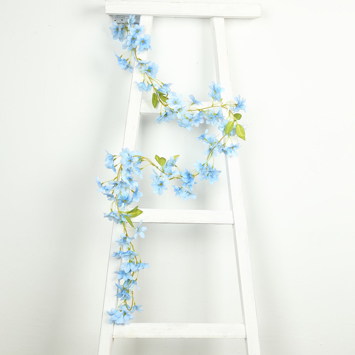 Blue jasmine silk flower garland with warm white LED lights on a white ladder.