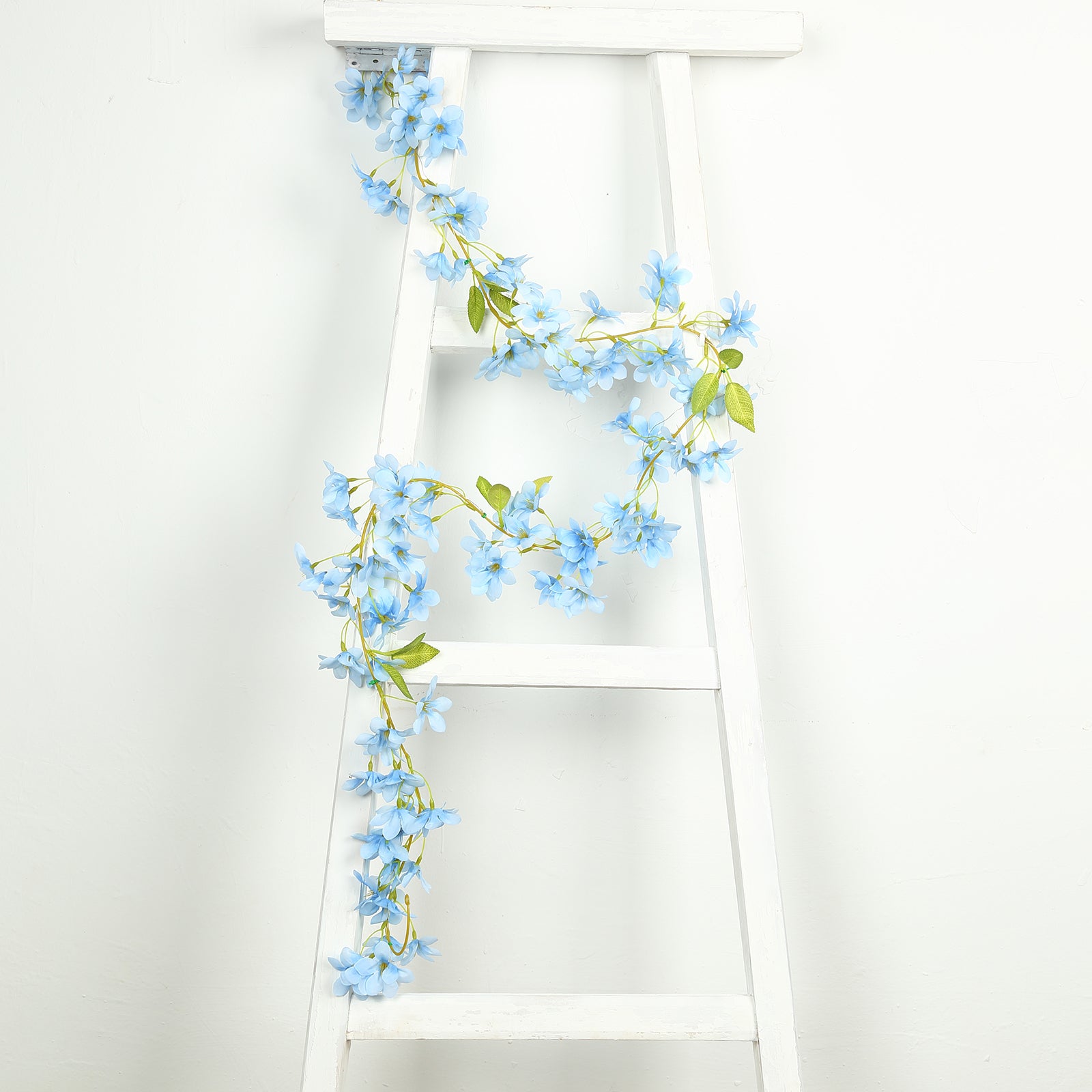 Blue jasmine silk flower garland with warm white LED lights on a white ladder.