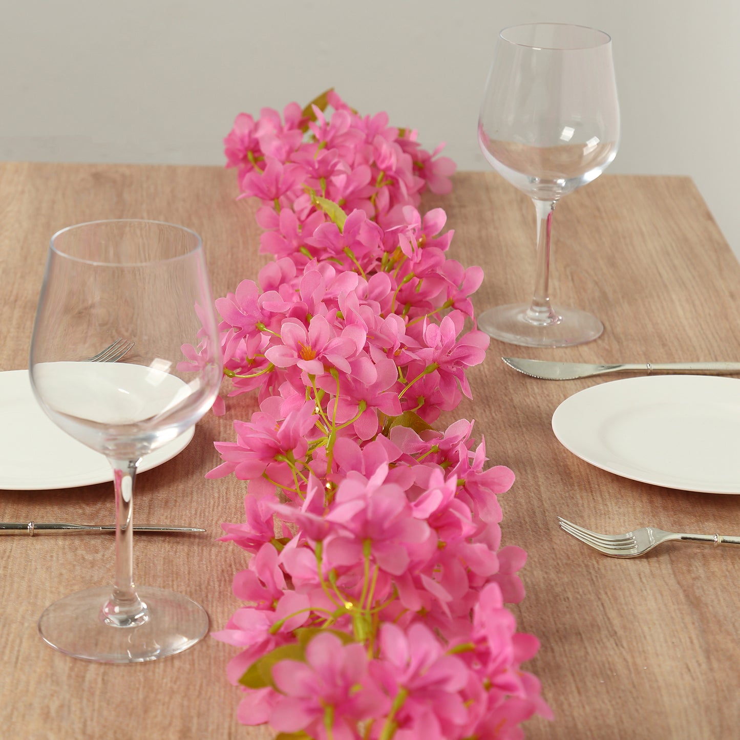 Pink jasmine silk flower garland with warm white LED lights on a wooden table.