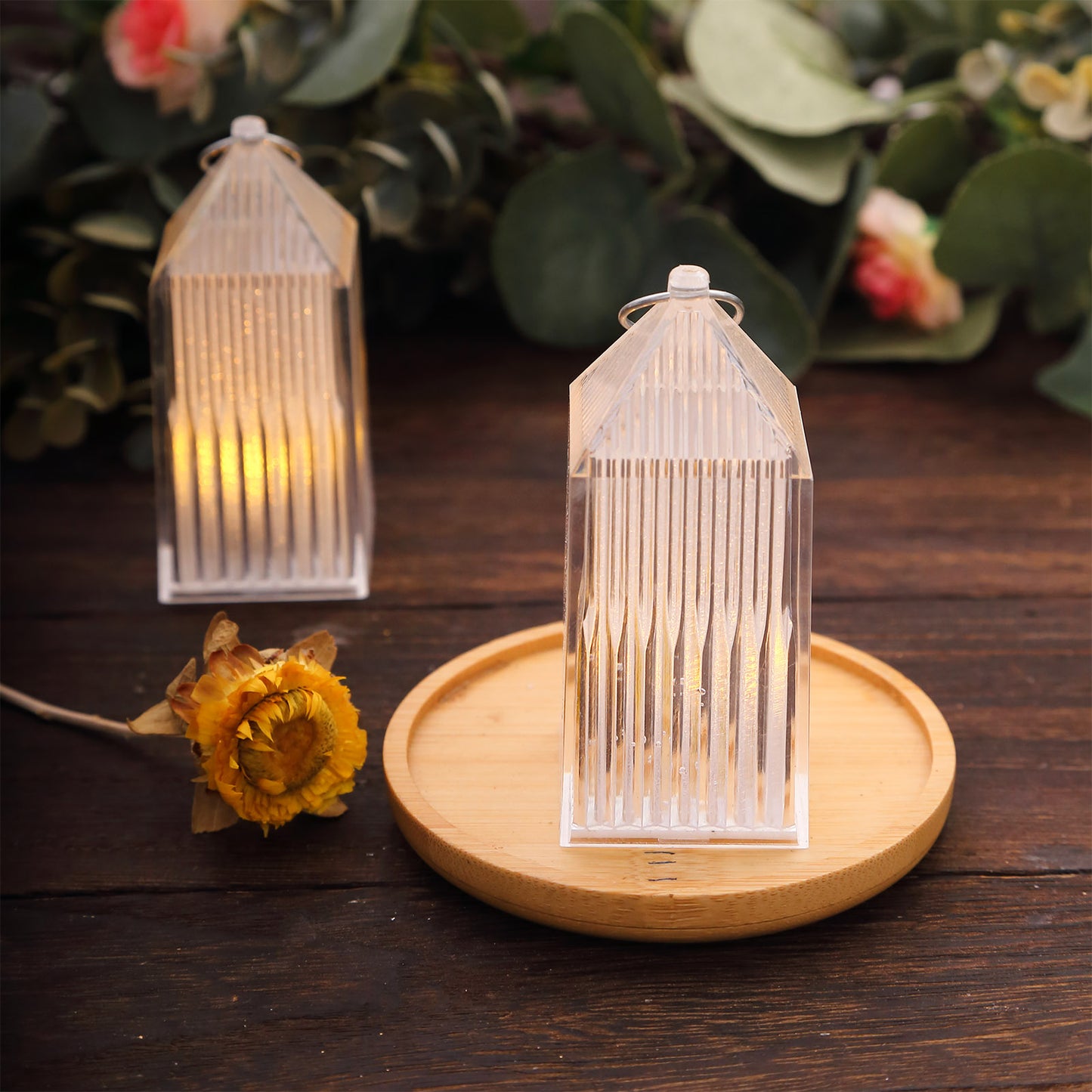 Clear warm white mini lanterns on a wooden tray, surrounded by greenery.