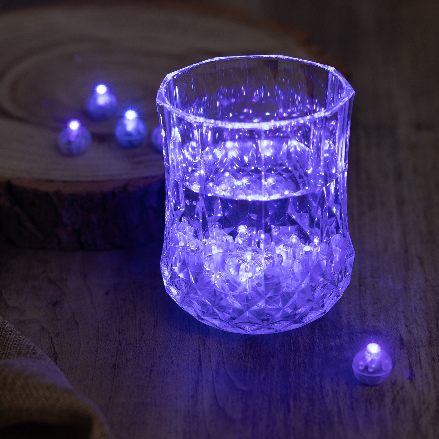 Light blue mini LED balls in a crystal glass with a wooden background.