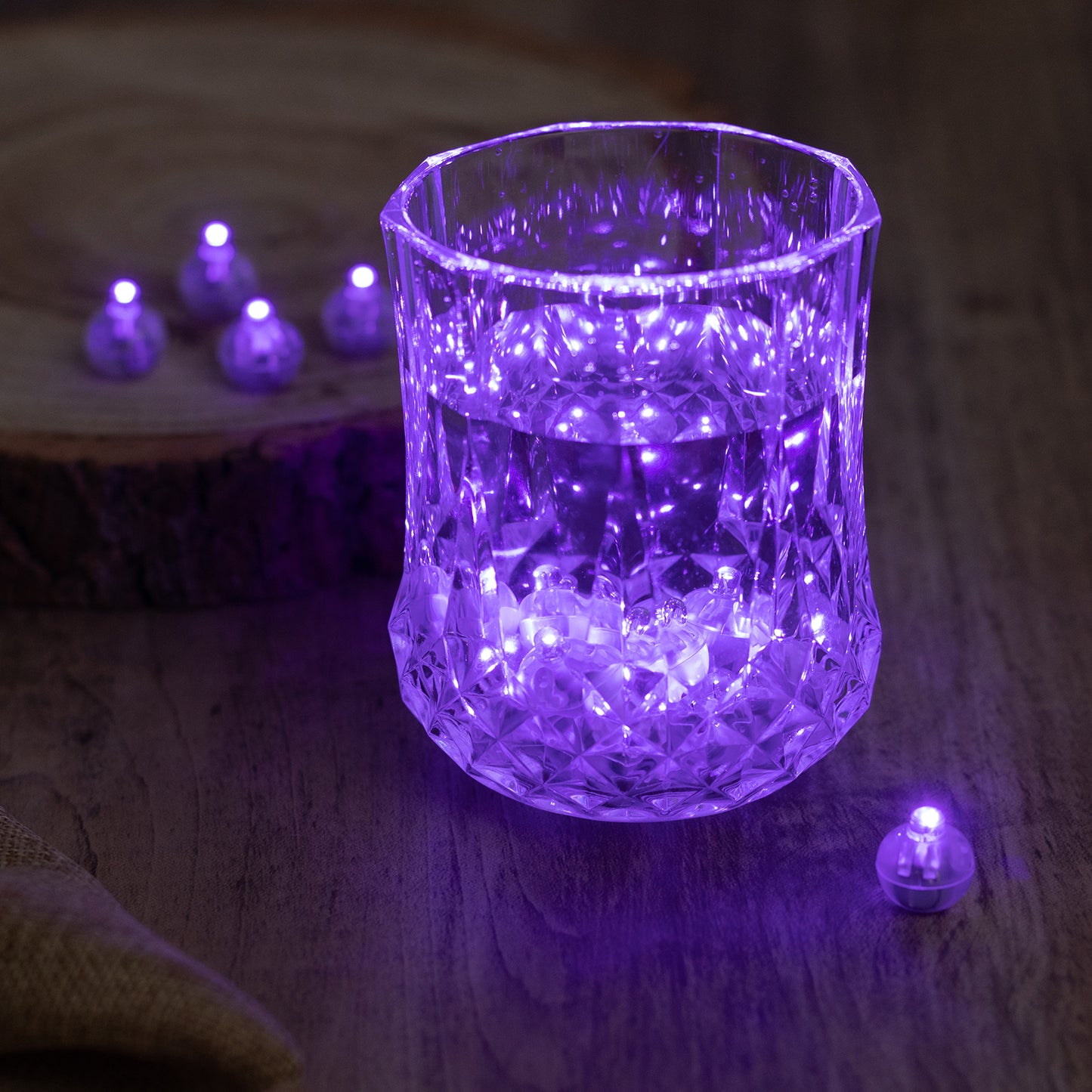 Purple mini LED balls illuminating a glass with water.