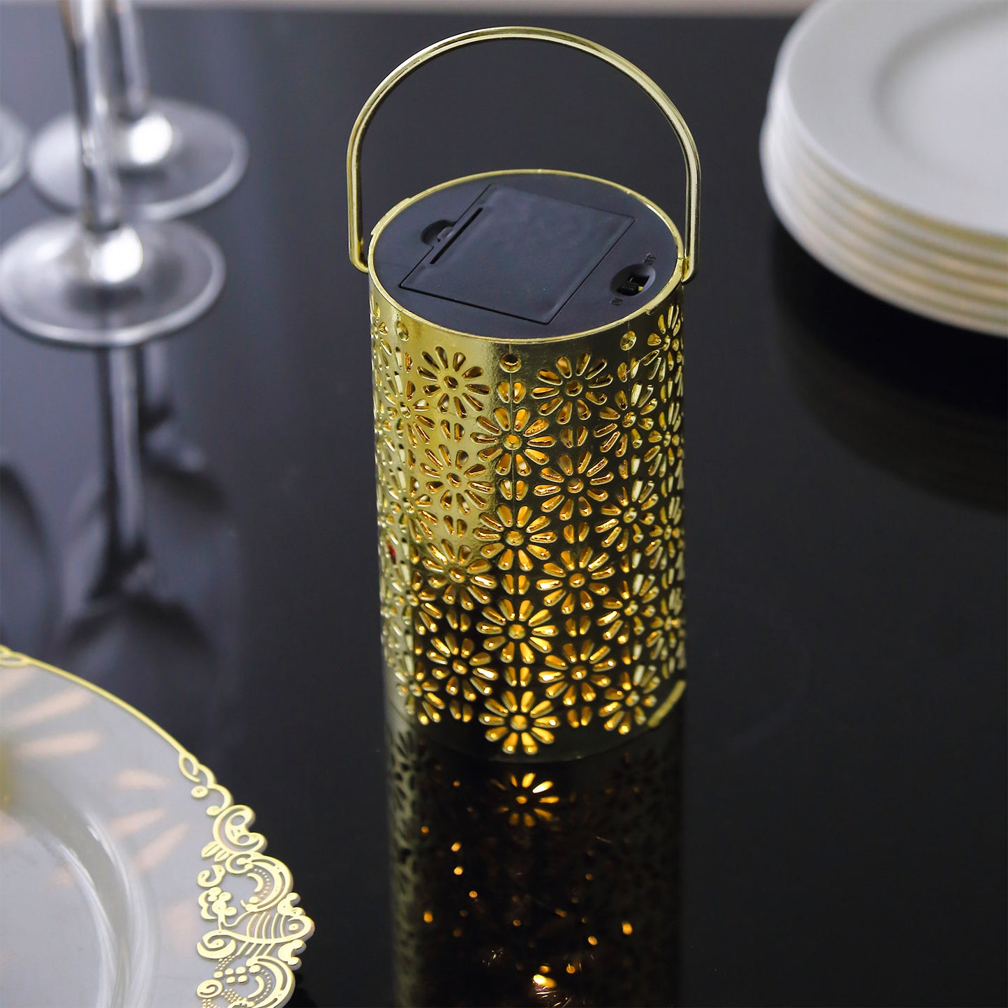 Gold LED lantern with flower design on a black table setting.
