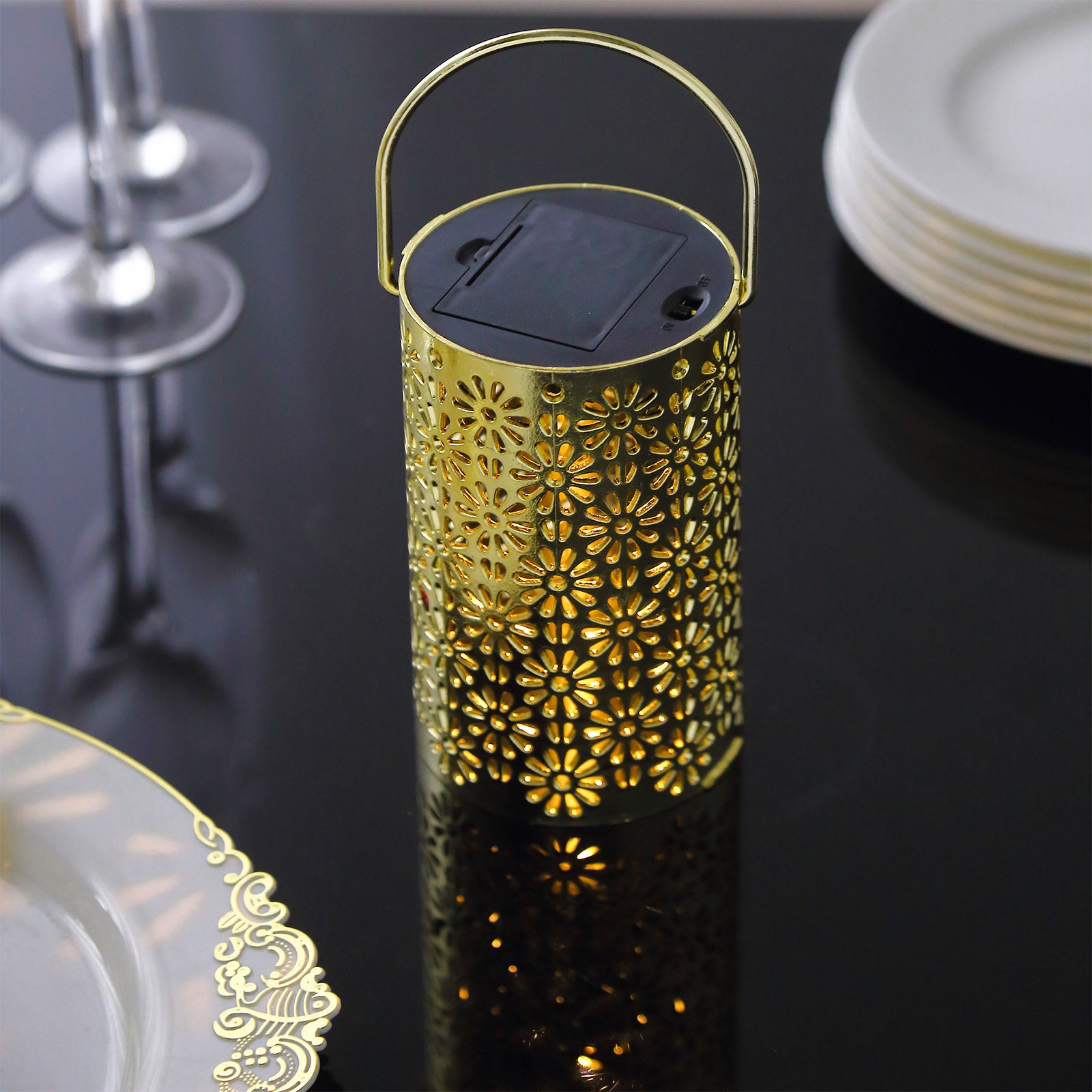 Gold LED lantern with flower design on a black table setting.