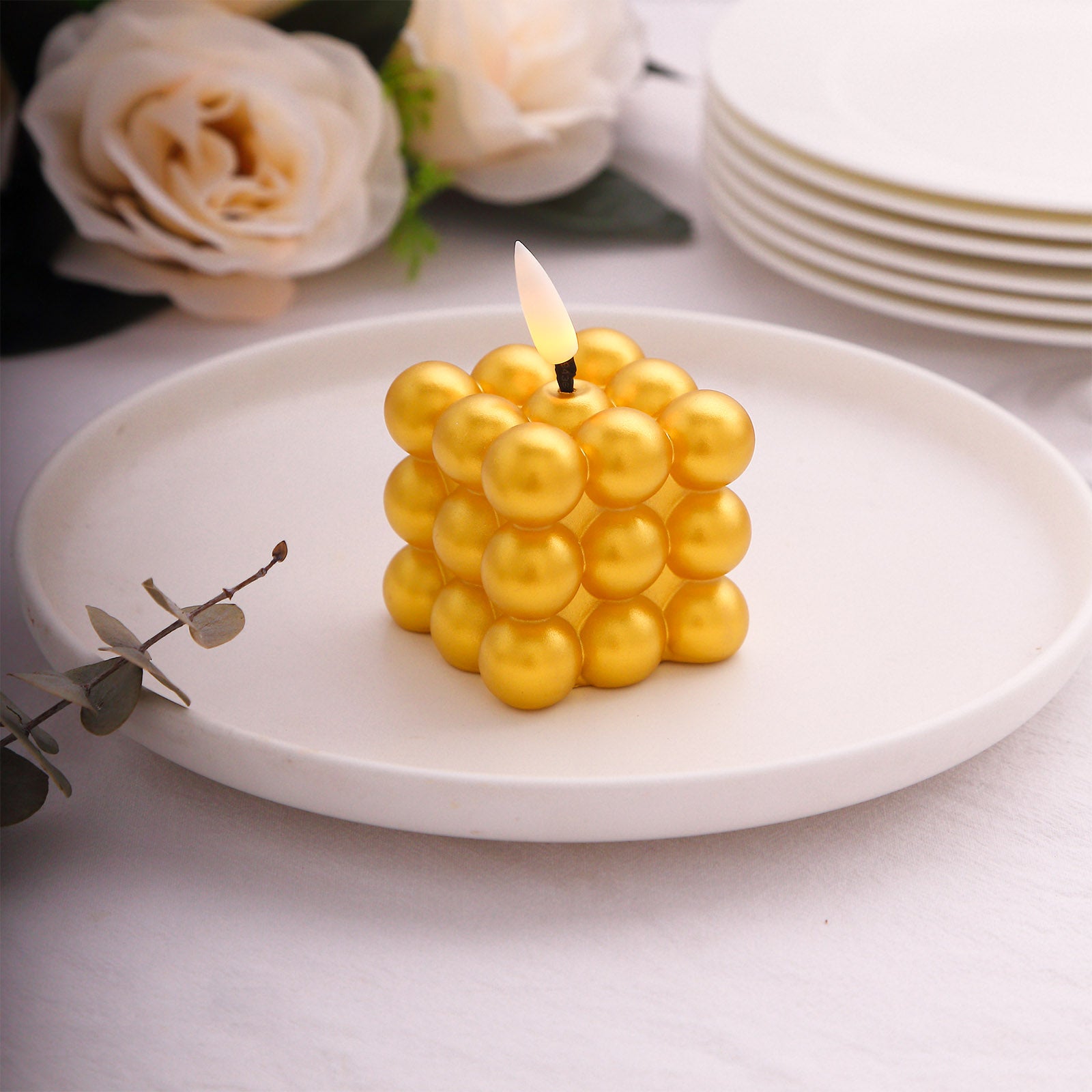 Metallic gold LED mini bubble candle on a white plate with flowers in the background.