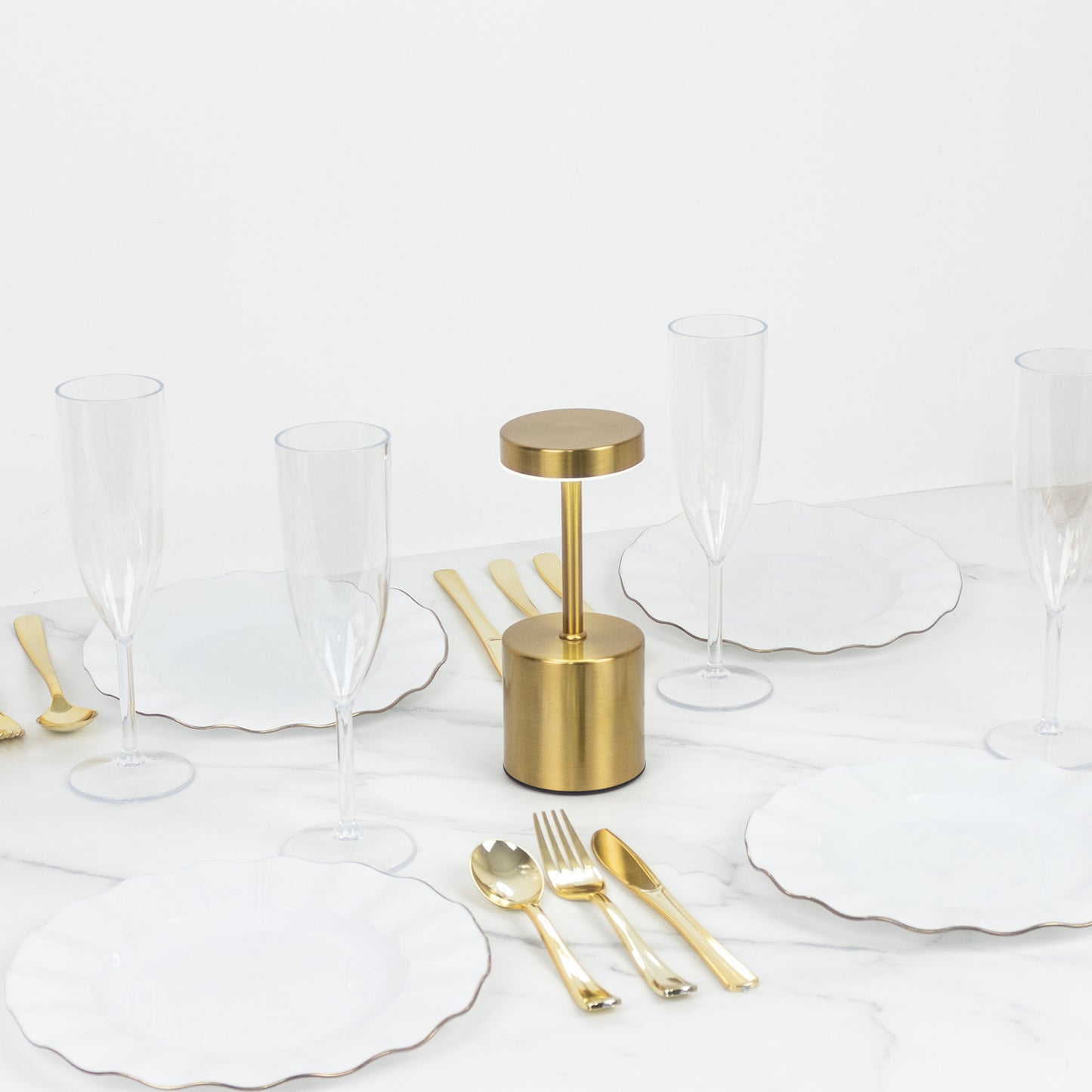 Gold metal LED table lamp on a dining table with white plates and glasses.