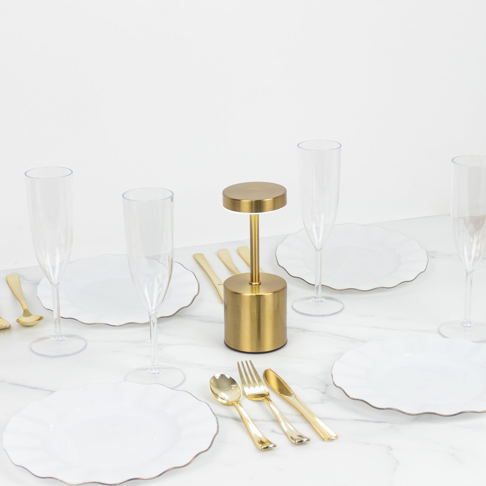 Gold metal LED table lamp on a dining table with white plates and glasses.