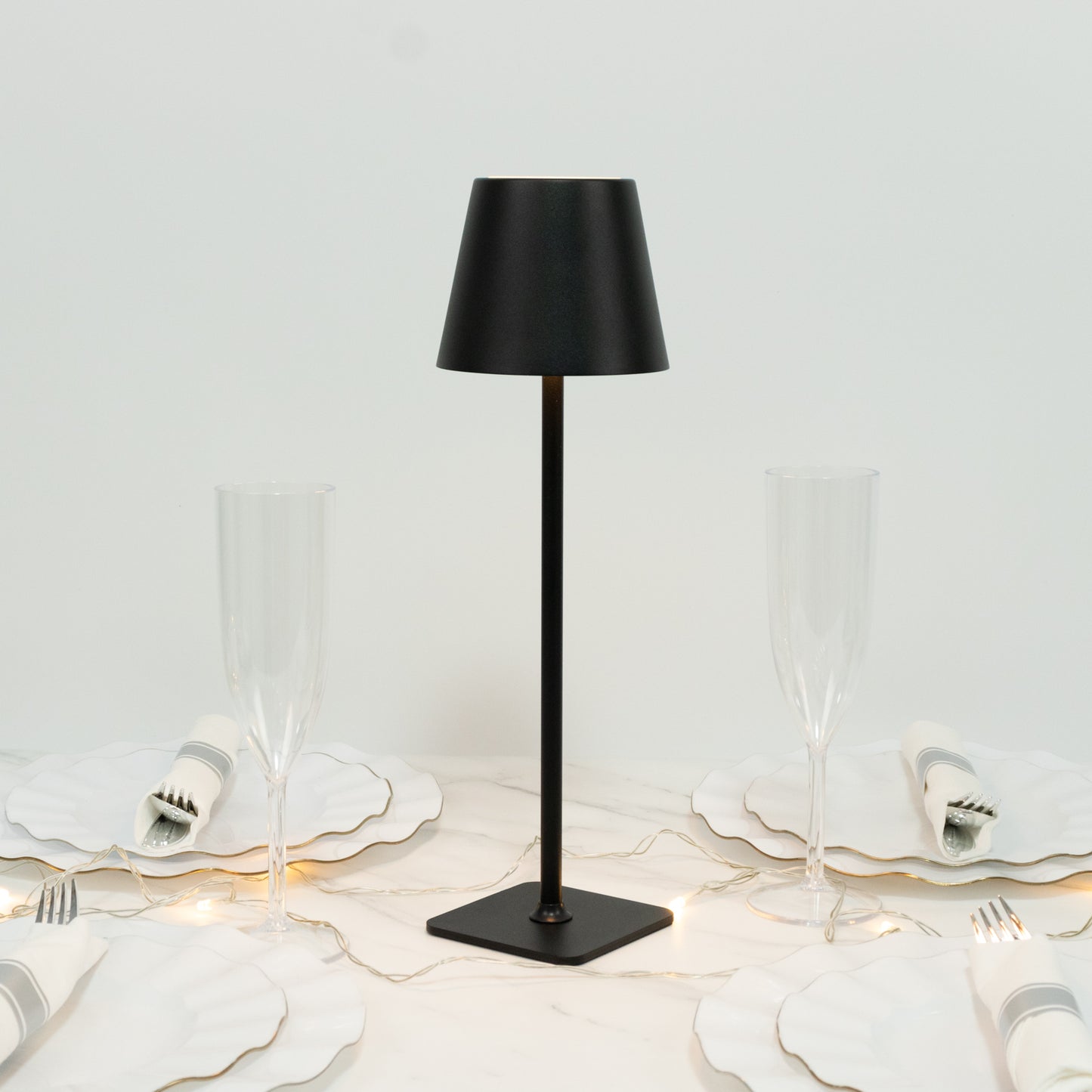 Black cordless table lamp with fluted shade on a dining table setting.