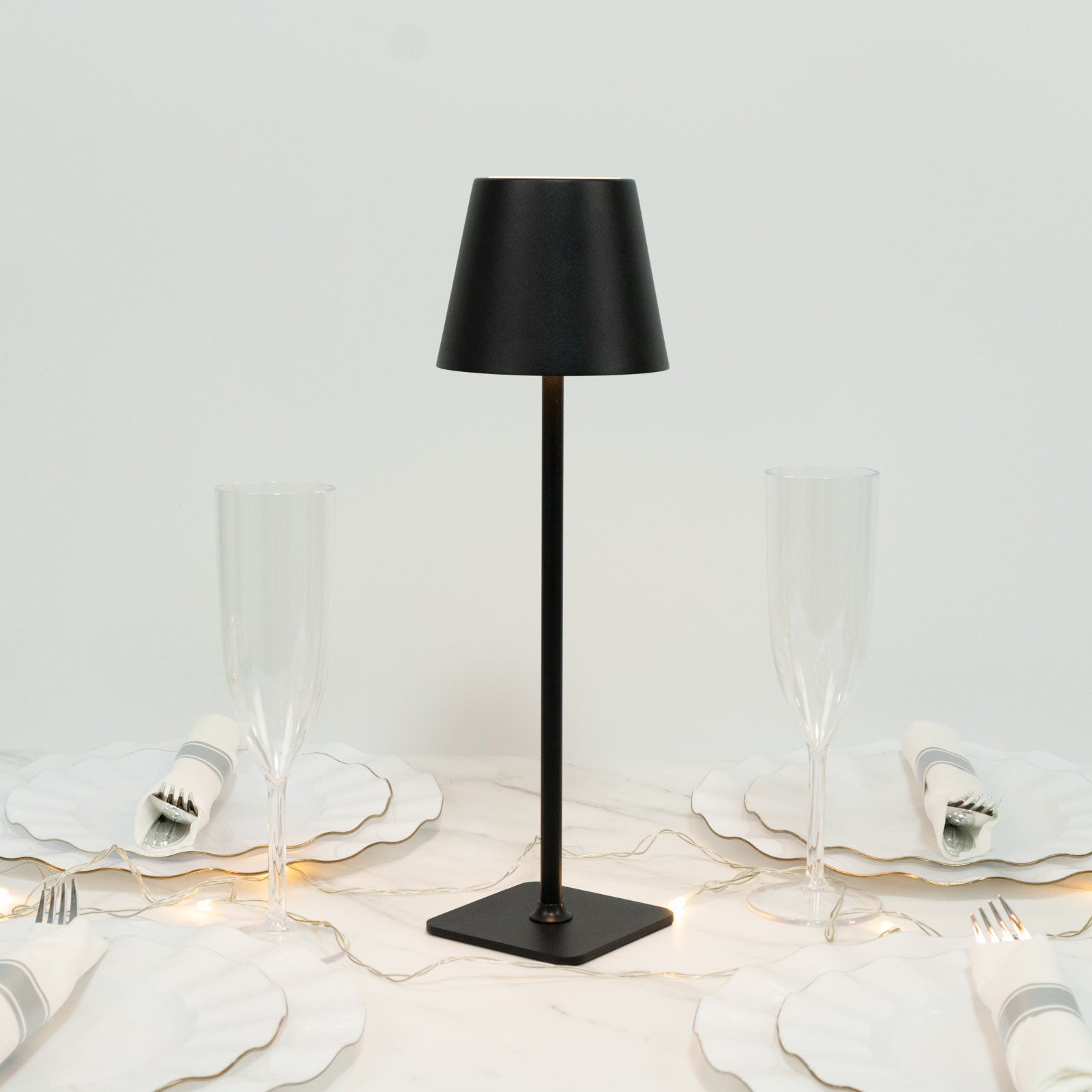Black cordless table lamp with fluted shade on a dining table setting.