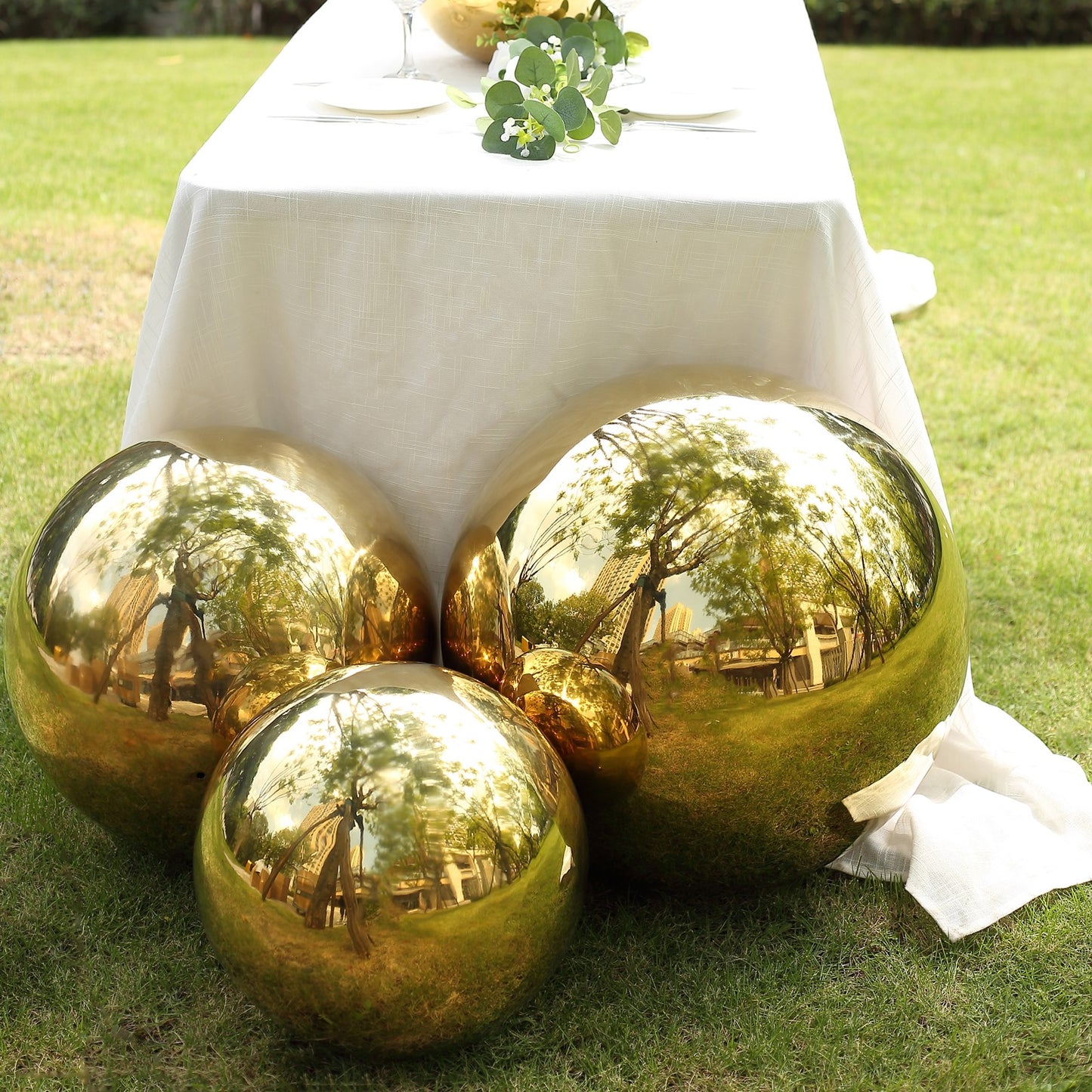 Gold reflective garden globe sphere on a table in a lush outdoor setting.