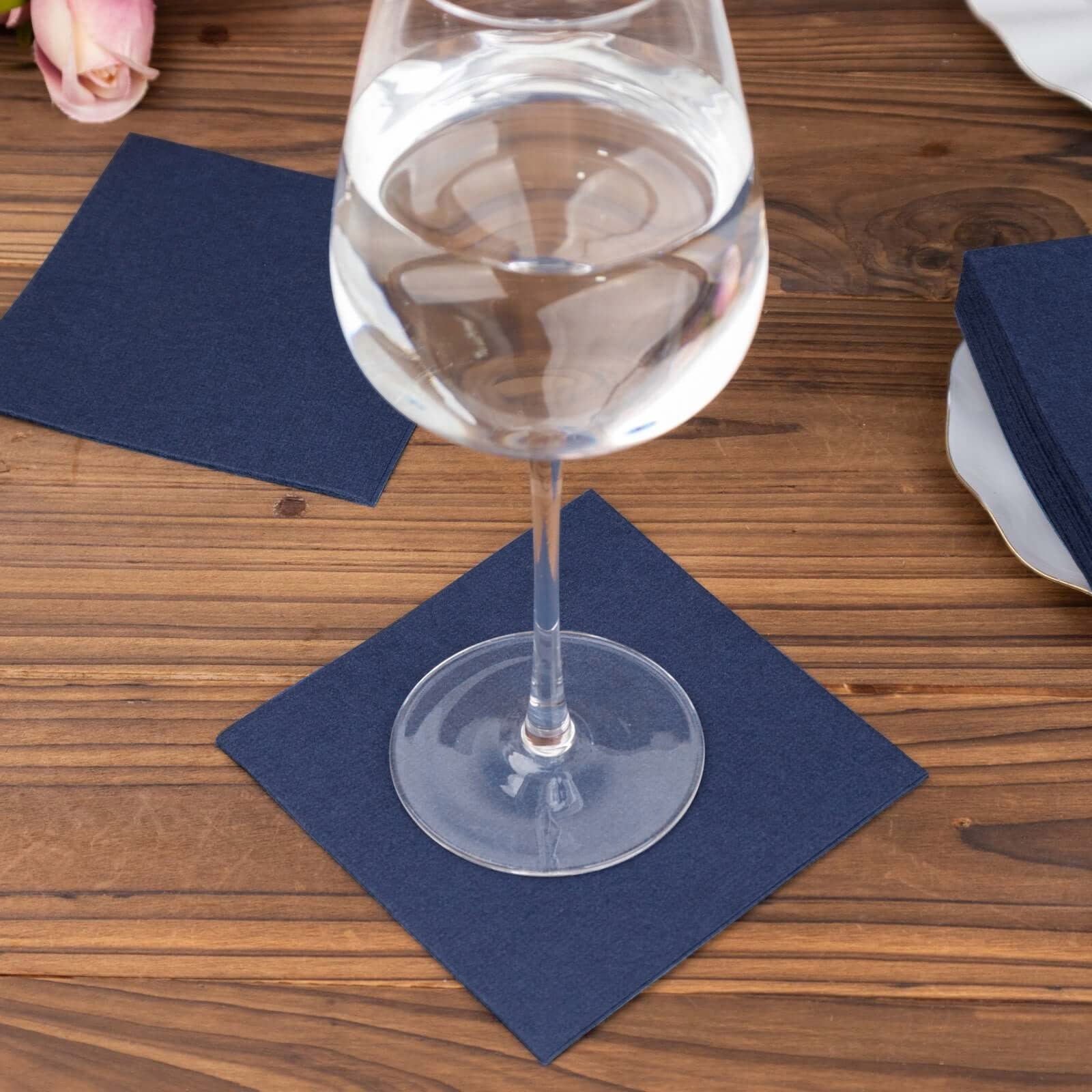 Navy blue linen-feel cocktail napkins under a glass on a wooden table.
