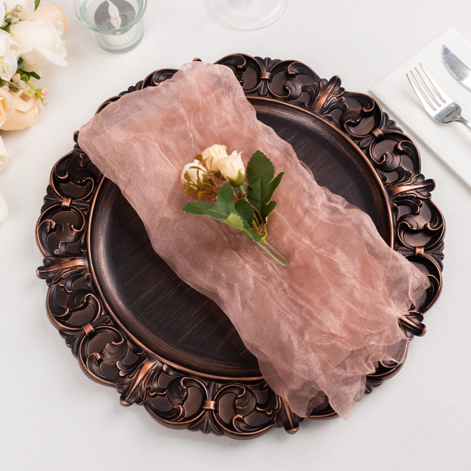 Dusty rose sheer crinkled organza dinner napkin on an ornate plate.