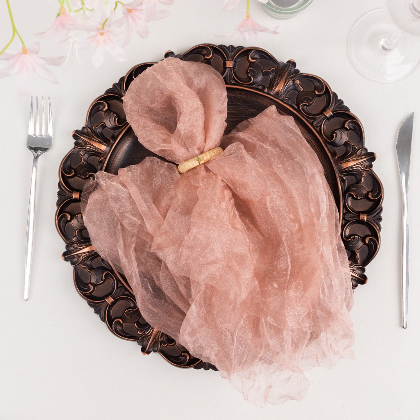 Dusty rose sheer crinkled organza dinner napkin on an ornate plate.