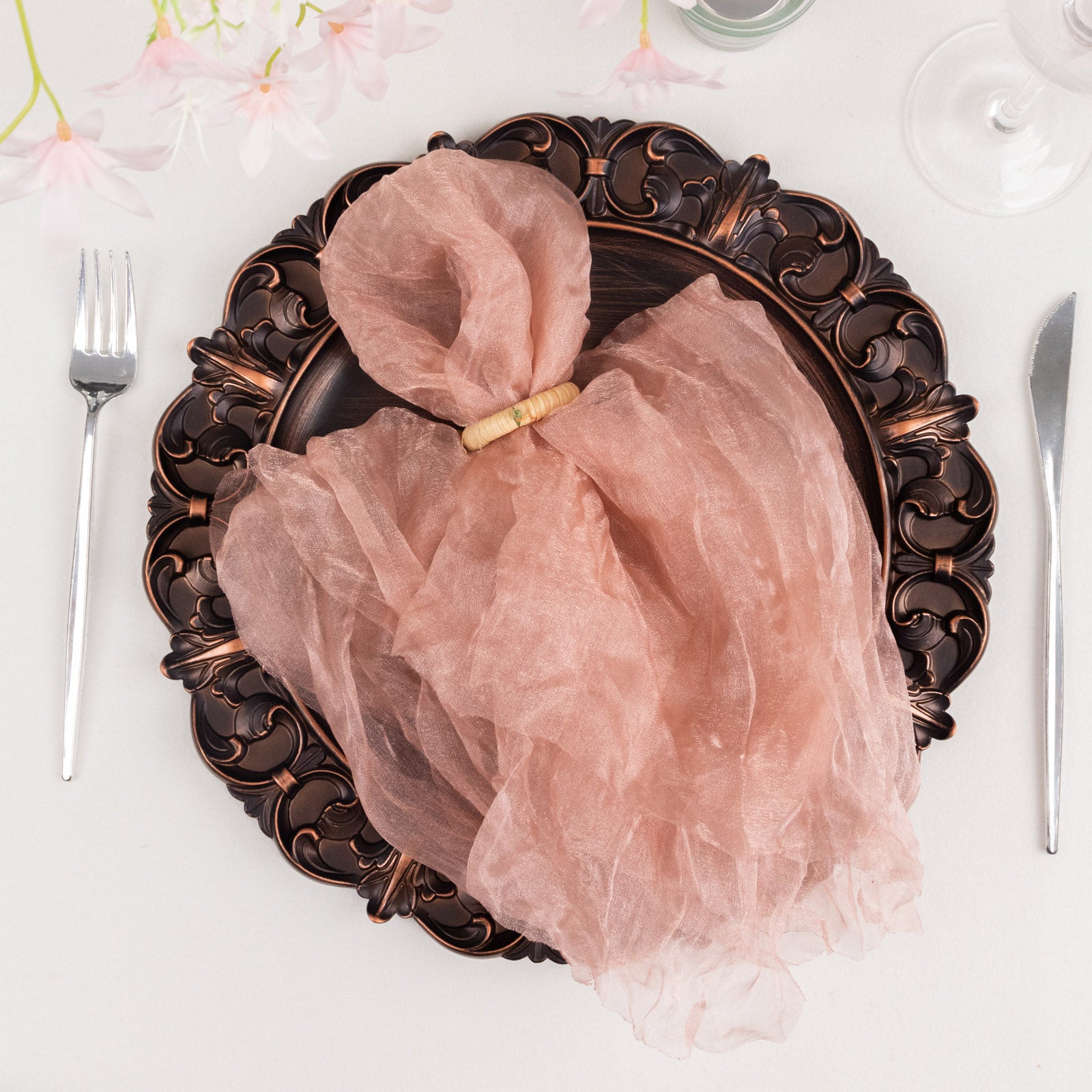 Dusty rose sheer crinkled organza dinner napkin on an ornate plate.