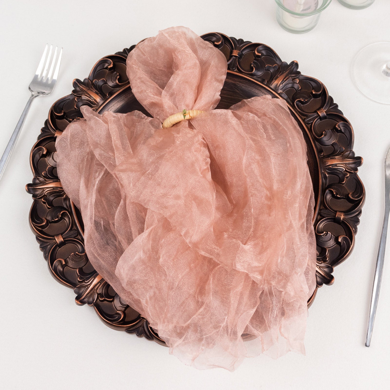 Dusty rose sheer crinkled organza dinner napkin on a decorative plate.