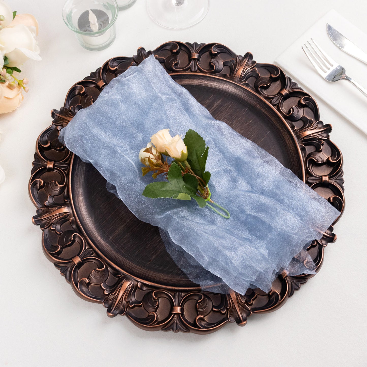 Dusty blue sheer crinkled organza dinner napkin on an ornate plate.