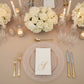 White napkin with gold foil monogram "S" on an elegant dining table setting.