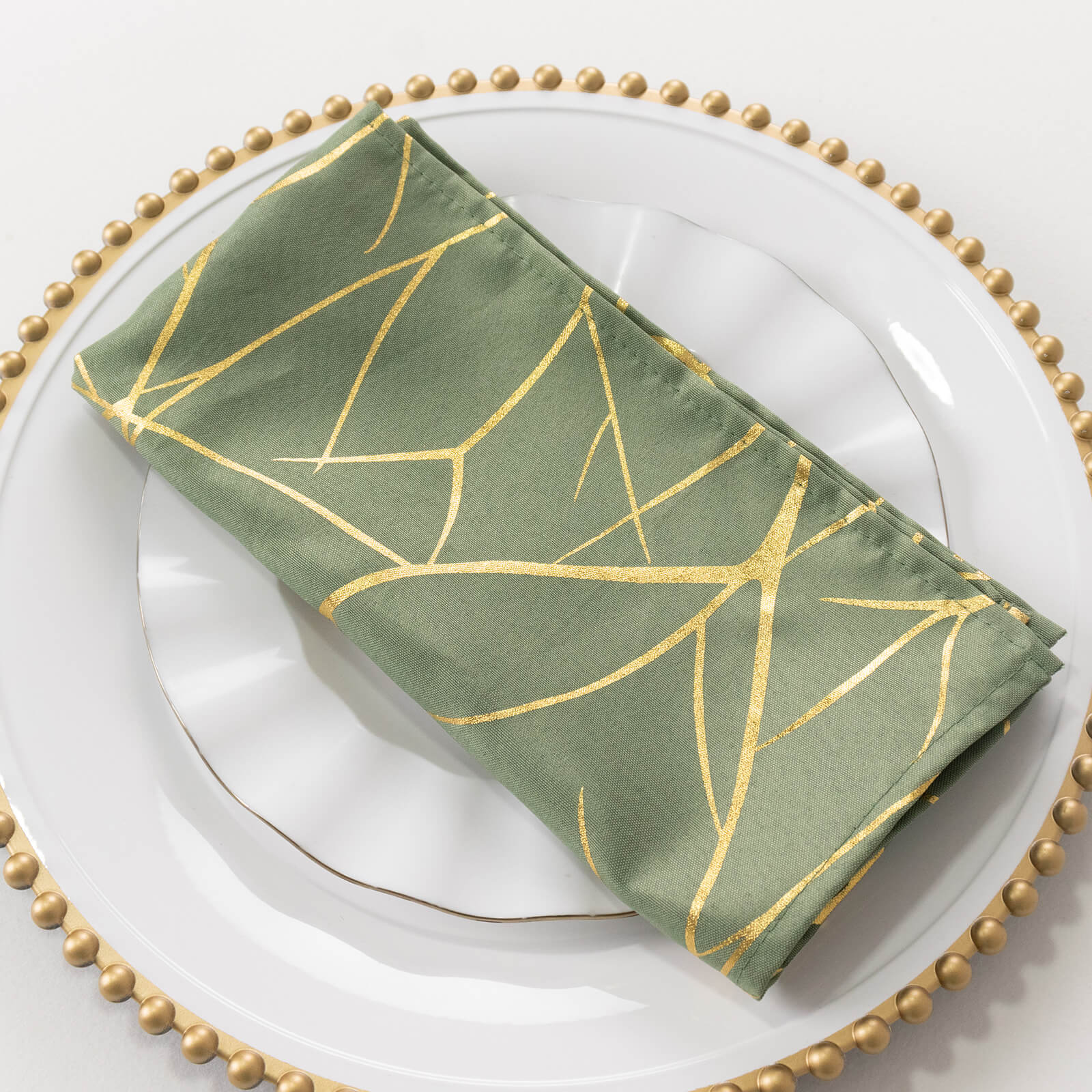 Dusty sage green cloth dinner napkin with gold foil tree branch pattern.
