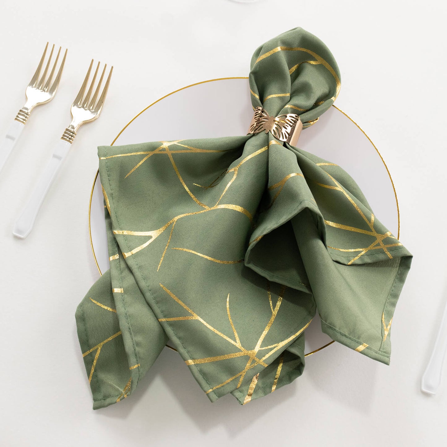 Dusty sage green napkin with gold foil tree branch pattern on a plate.