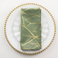 Dusty sage green dinner napkin with gold foil tree branch pattern.