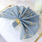 Modern dusty blue and geometric gold dinner napkin on a table setting.