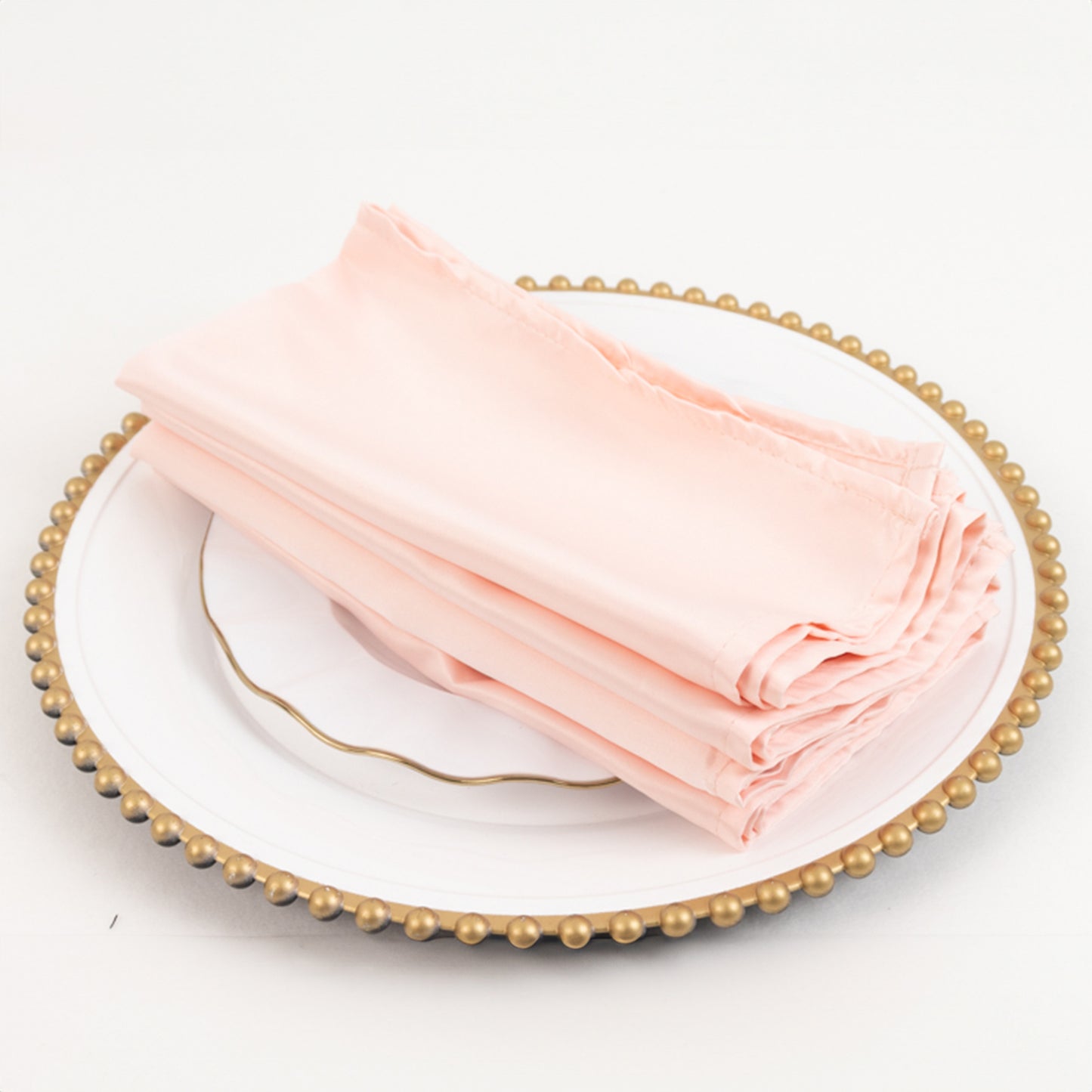 Blush satin napkins stacked on a decorative plate.