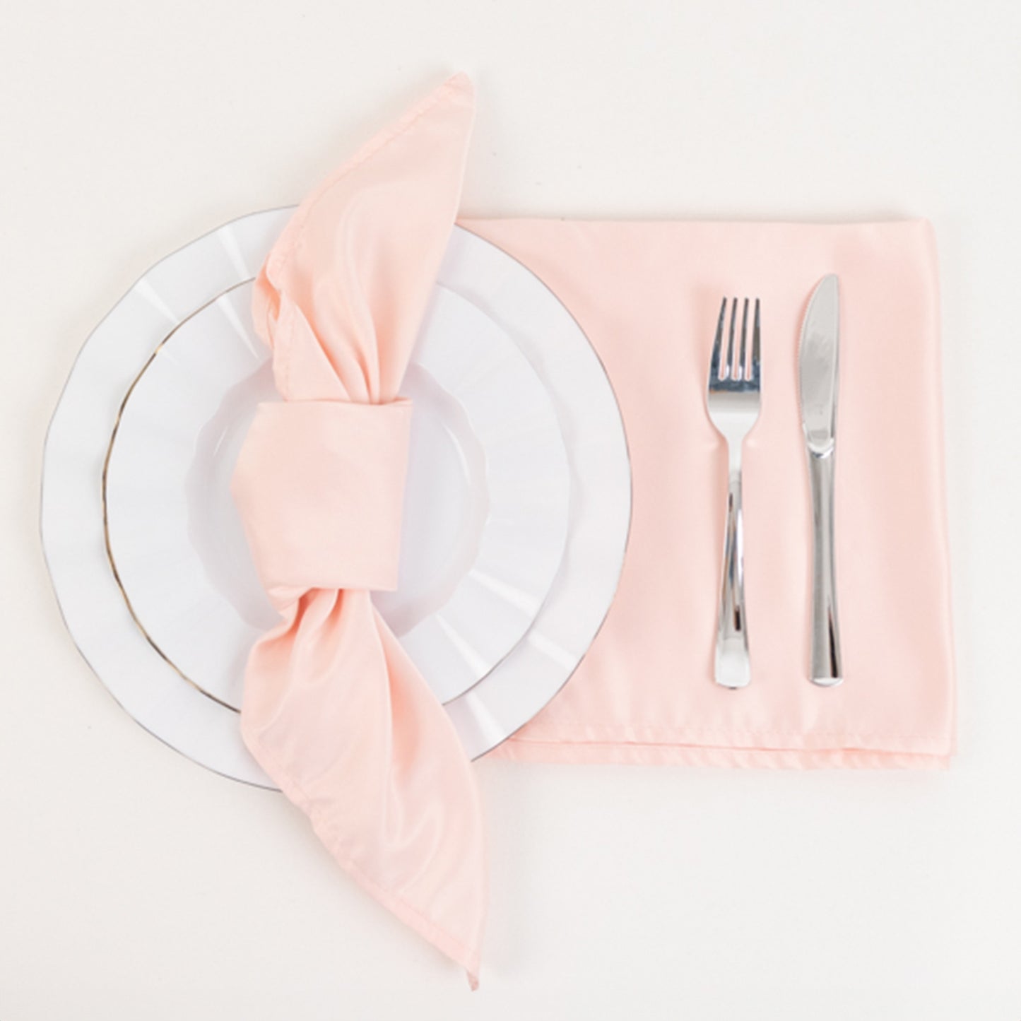Blush satin napkins on a white plate with silver utensils.