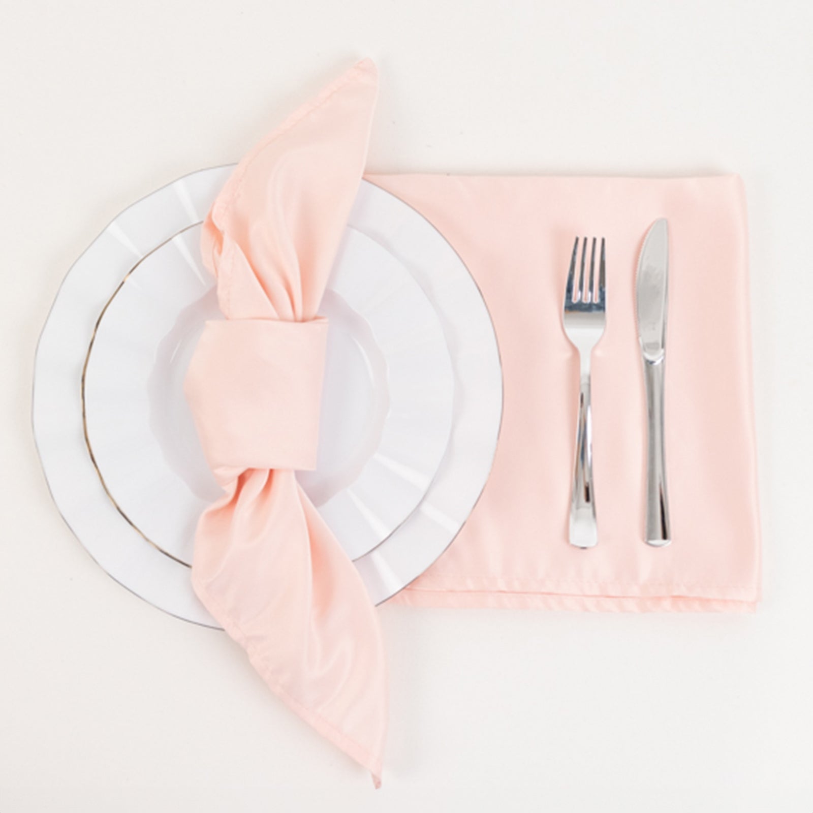 Blush satin napkins on a white plate with silver utensils.