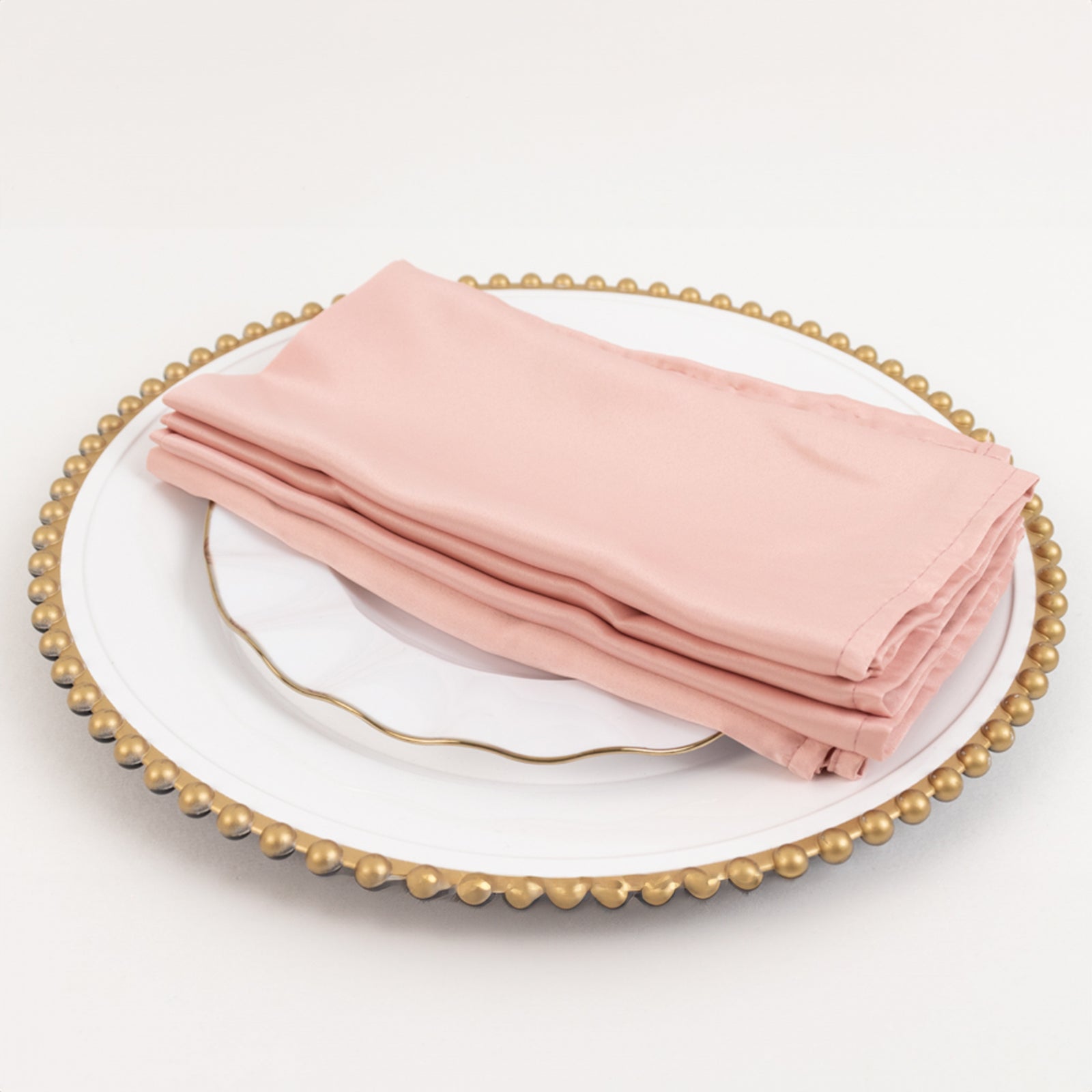 Dusty rose satin napkins stacked on a decorative plate.