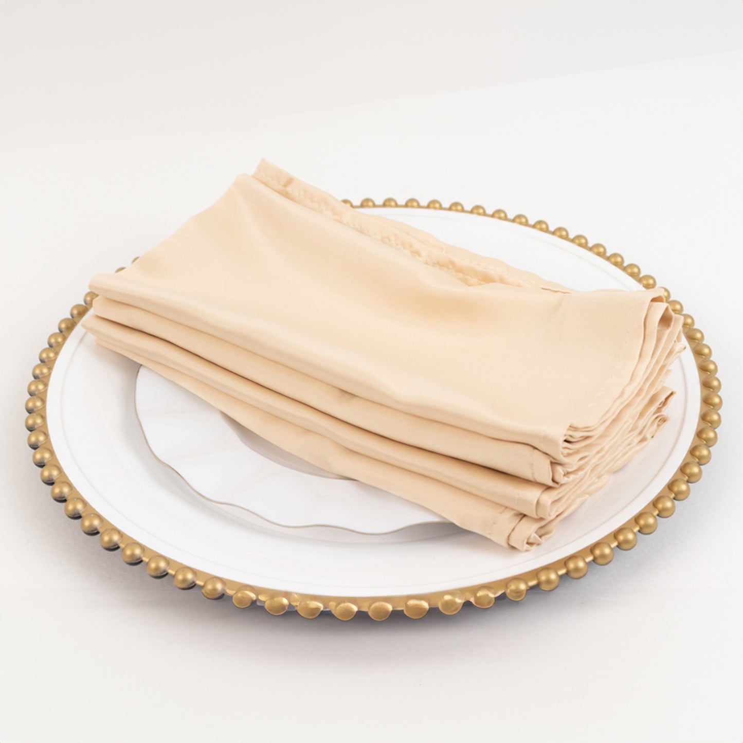 Beige satin napkins stacked elegantly on a decorative plate.