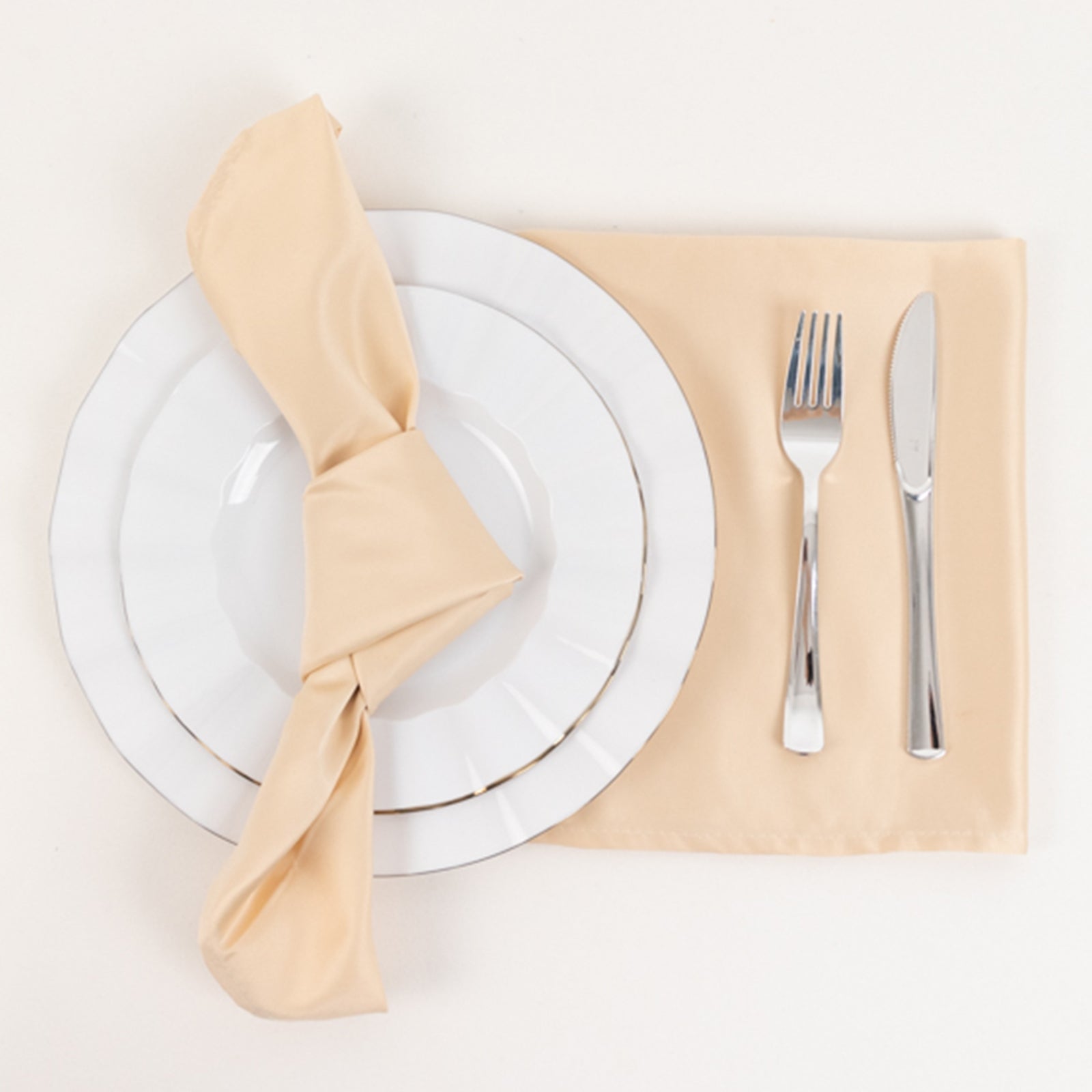 Beige satin napkins on a table setting with plate and cutlery.
