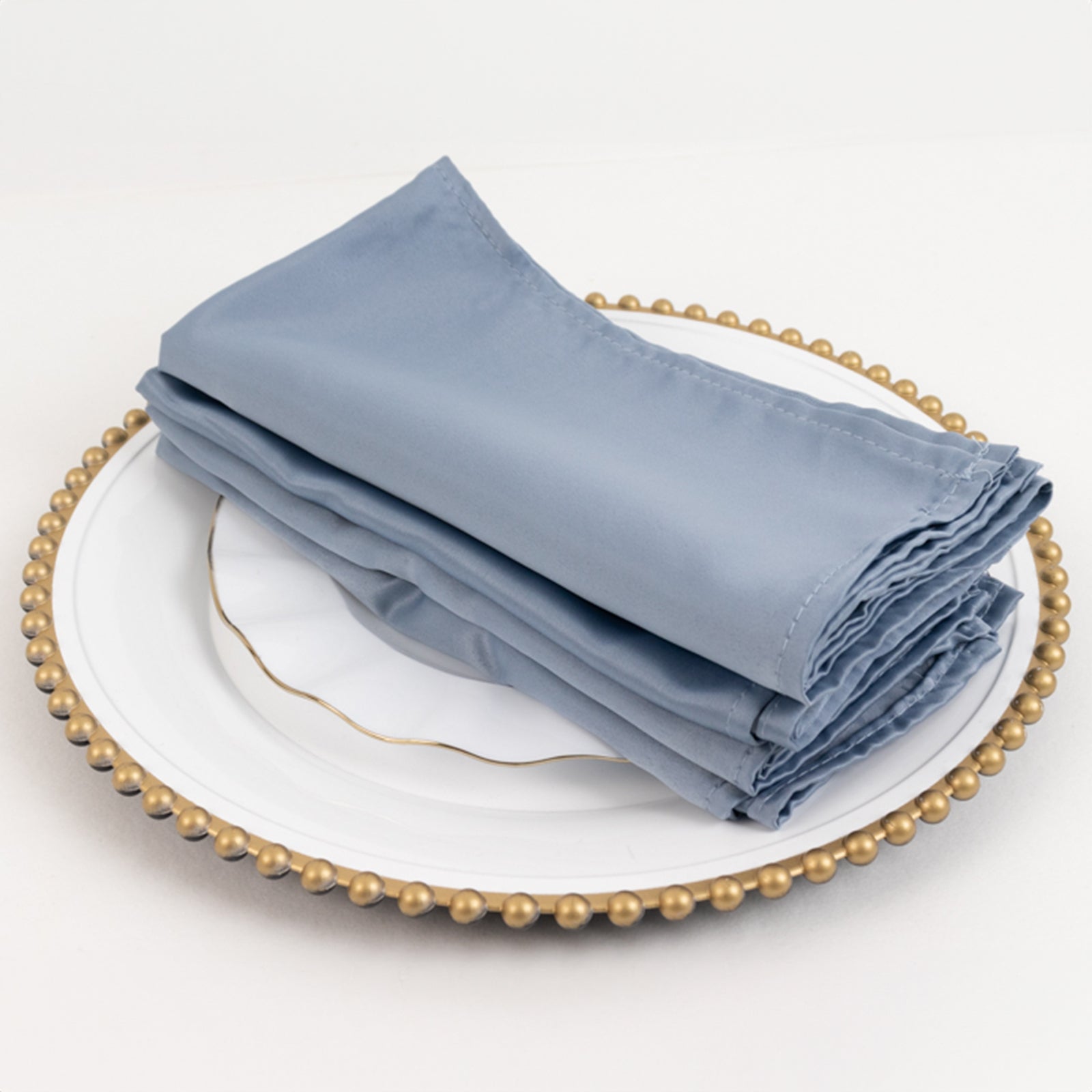 Dusty blue satin napkins stacked on a decorative plate.