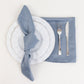 Dusty blue satin napkin set with white plate and silver cutlery.