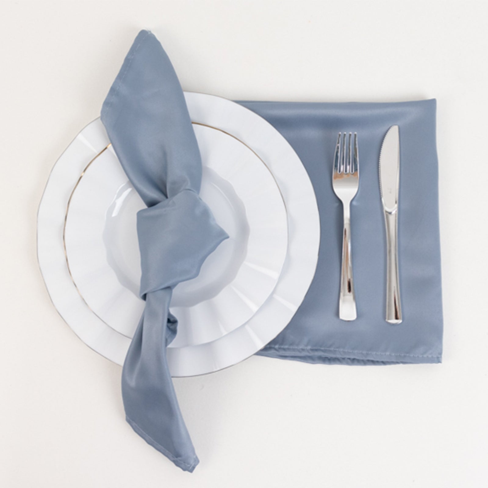Dusty blue satin napkin set with white plate and silver cutlery.