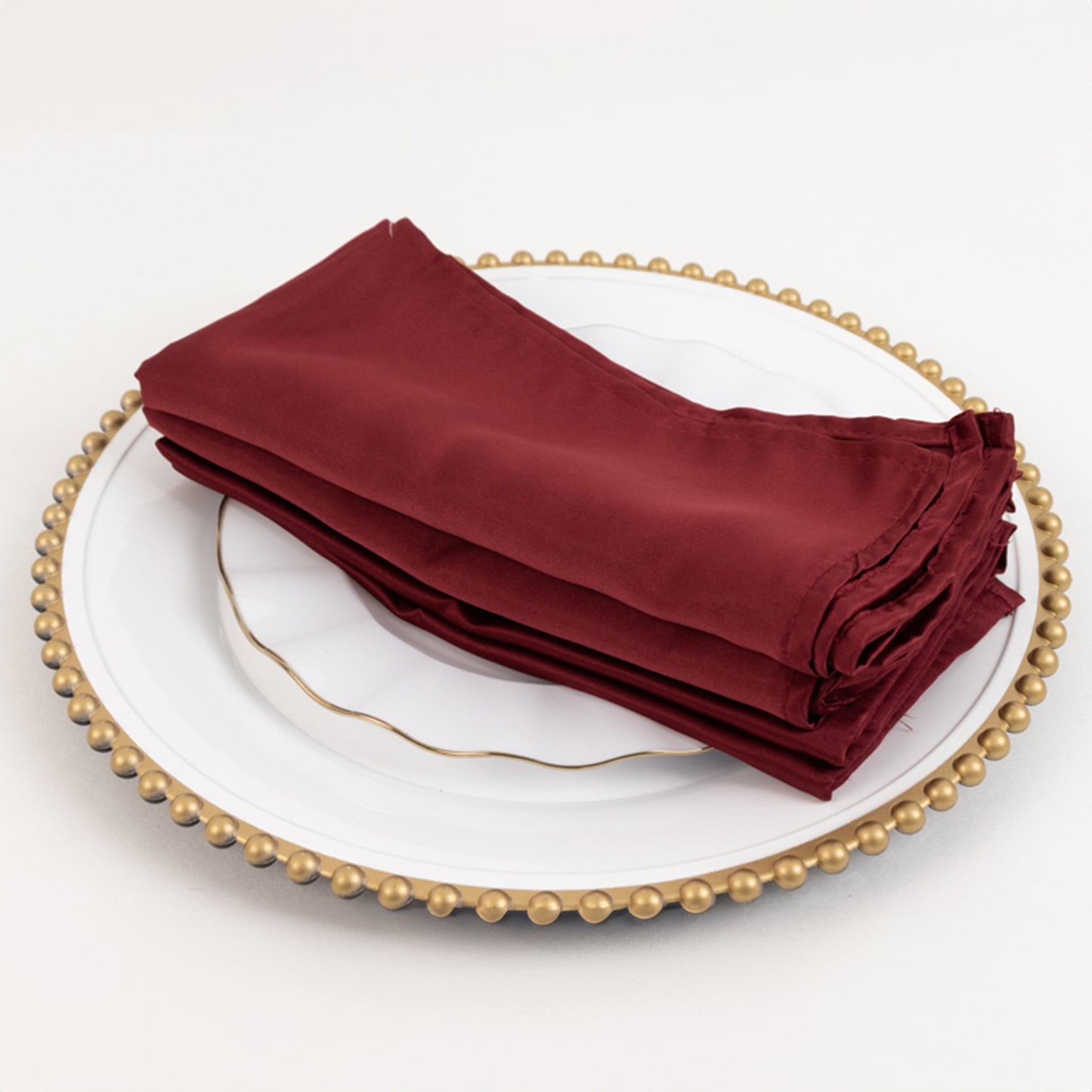 Burgundy satin napkins stacked on a decorative plate.